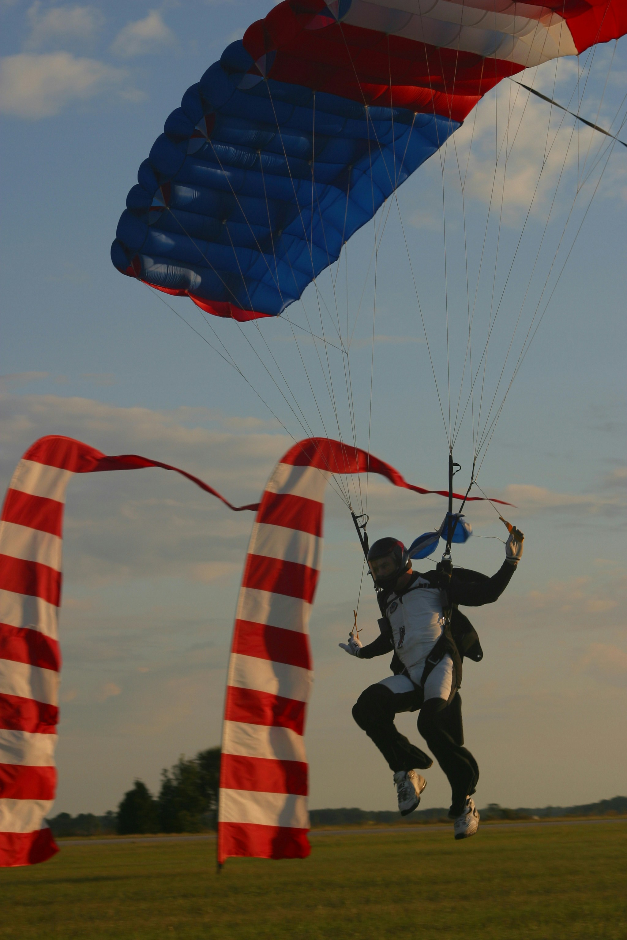 Un parachutiste atterrit près de balises au sol rayées.