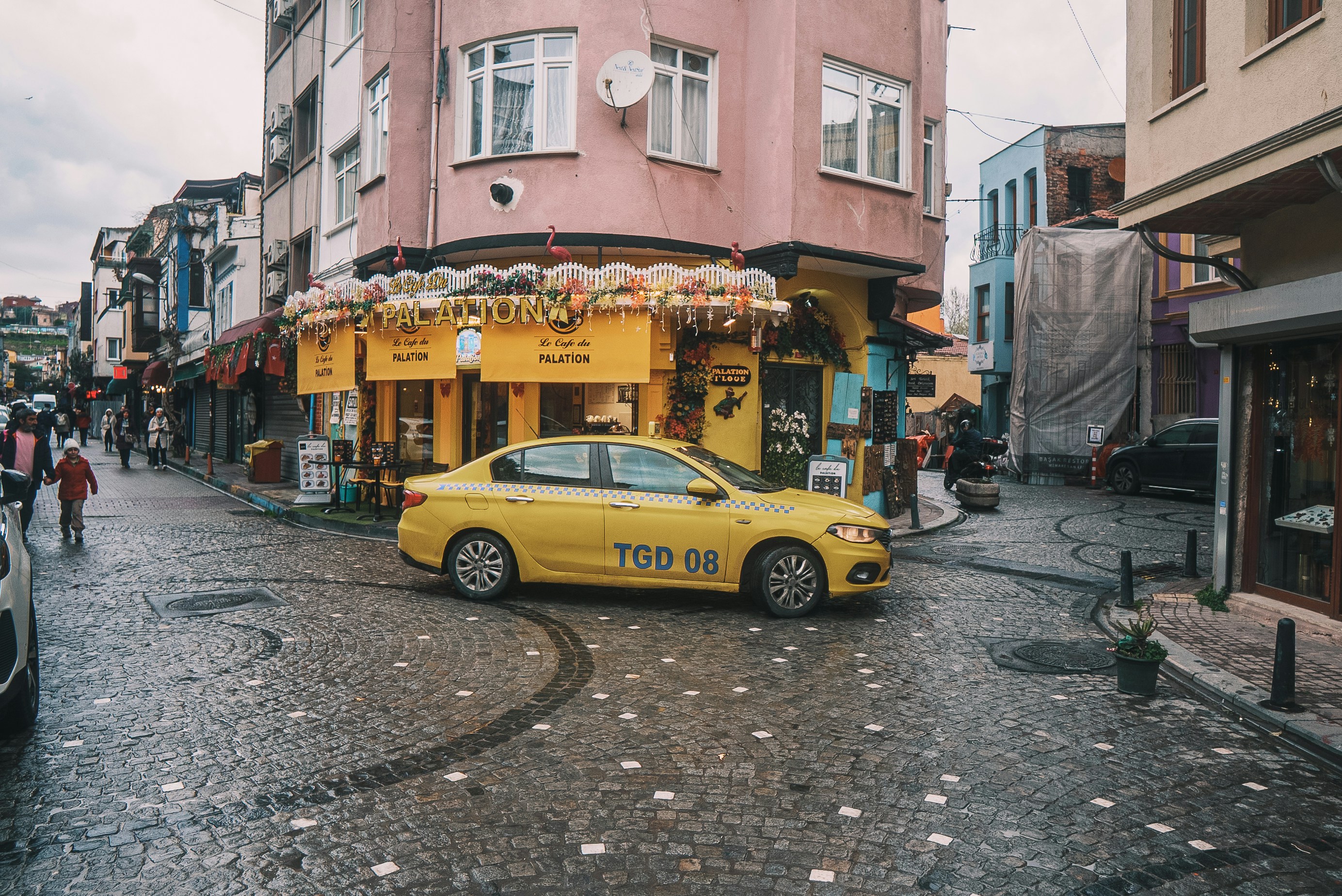 A yellow taxi drives through a busy city street.