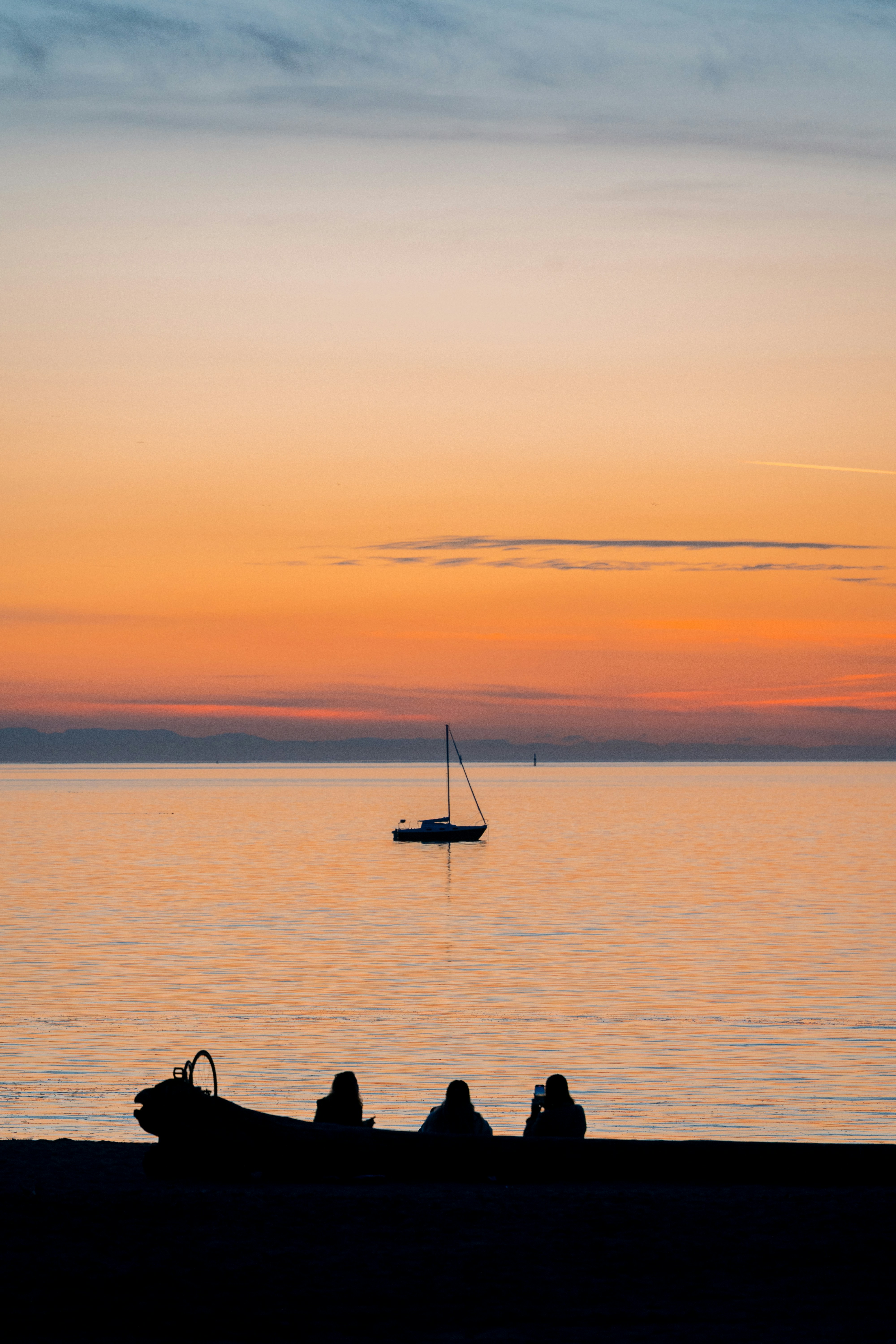 Silhouetted boat, people, and sailboat at sunset.