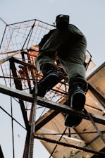 Someone climbs a tall, metal structure outdoors.