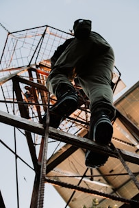 Someone climbs a tall, metal structure outdoors.