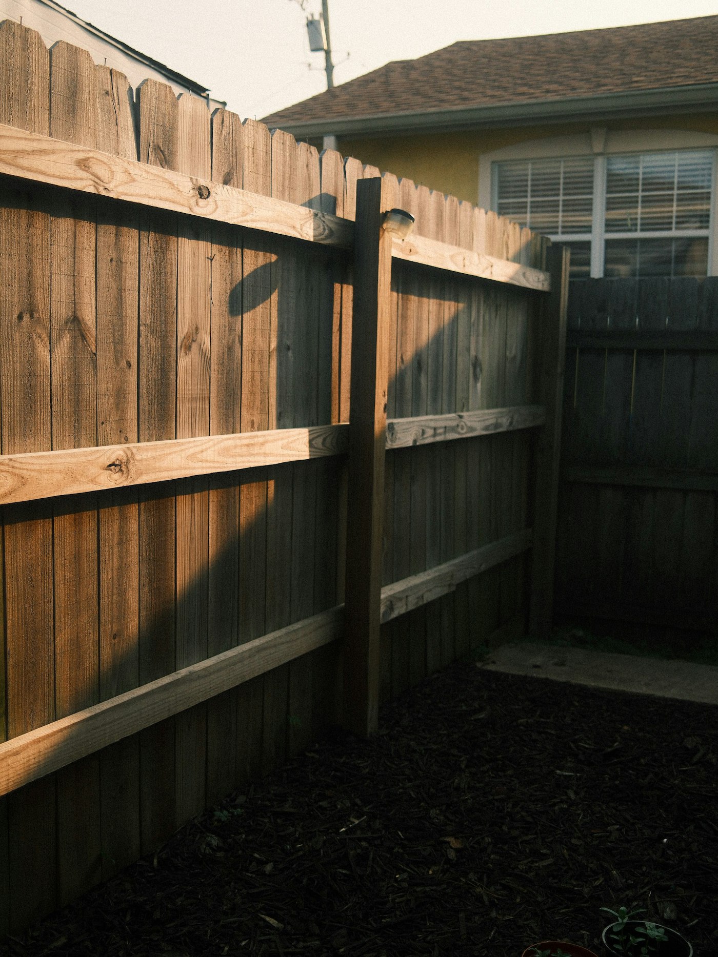 Back side of a wooden privacy fence showing posts and horizontal rails in a residential backyard