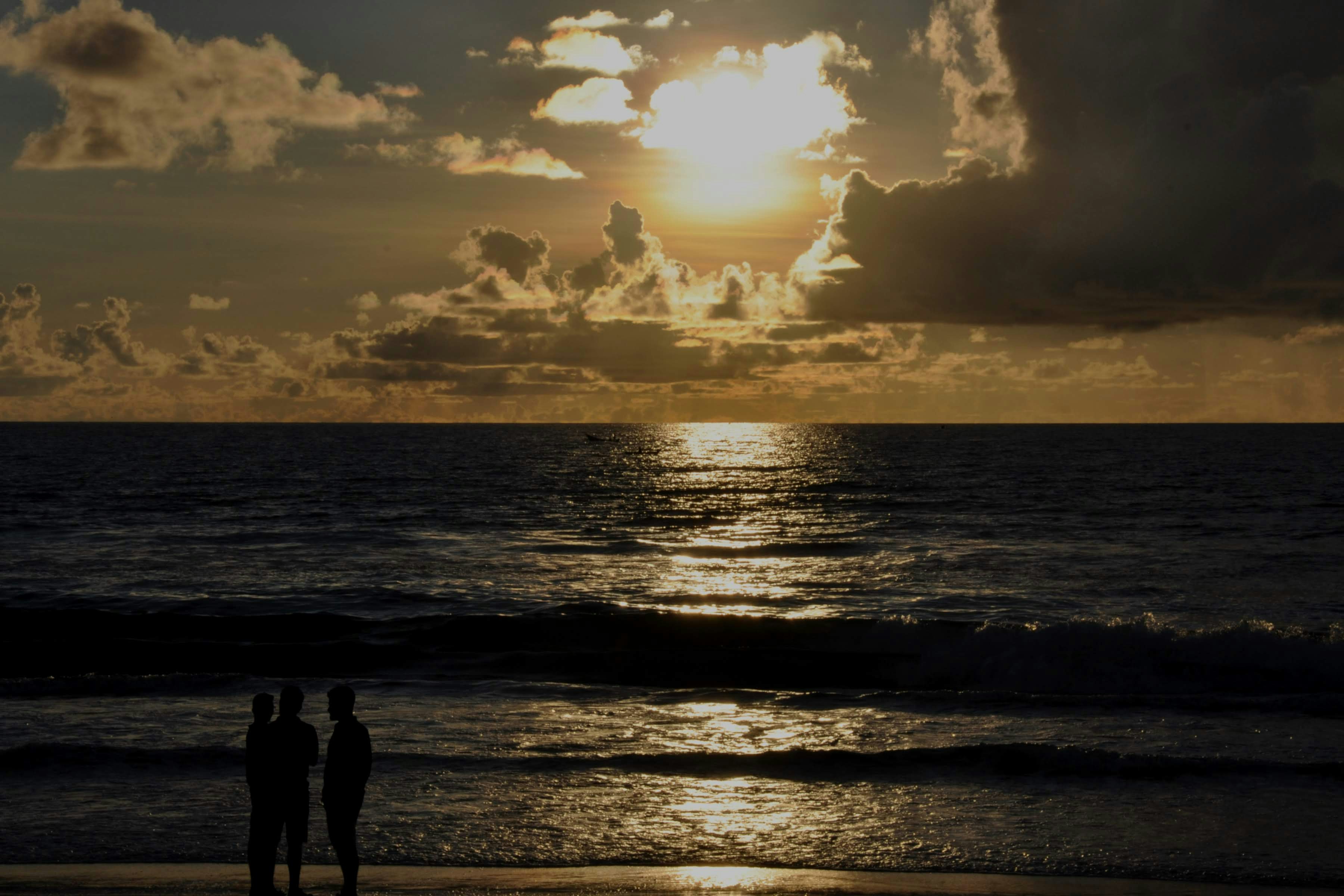 Sunset over the ocean with silhouettes of people.