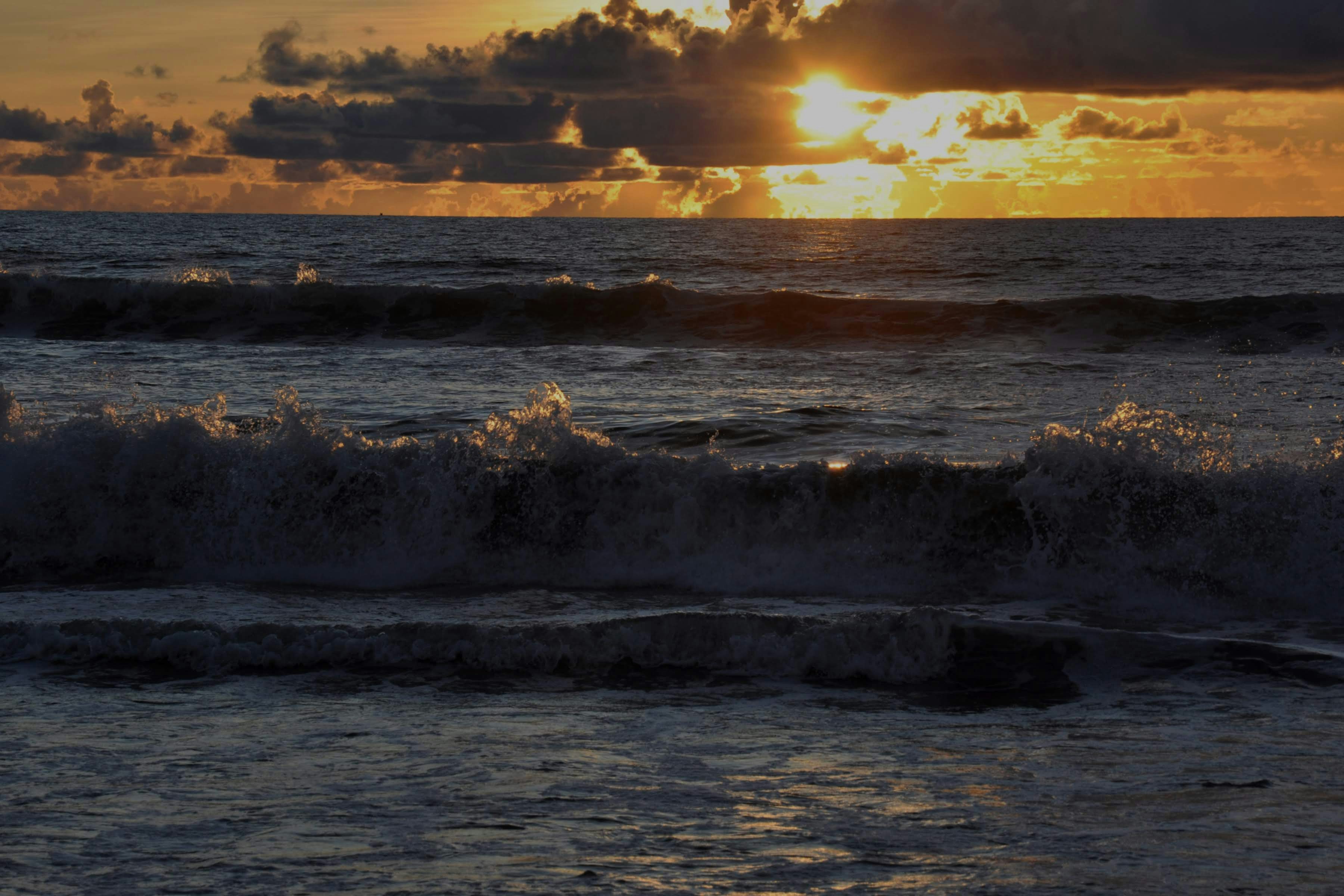 Waves crash against the shore during a golden sunset.