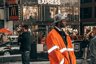 A person in orange coat stands on a busy street.