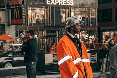 A person in orange coat stands on a busy street.