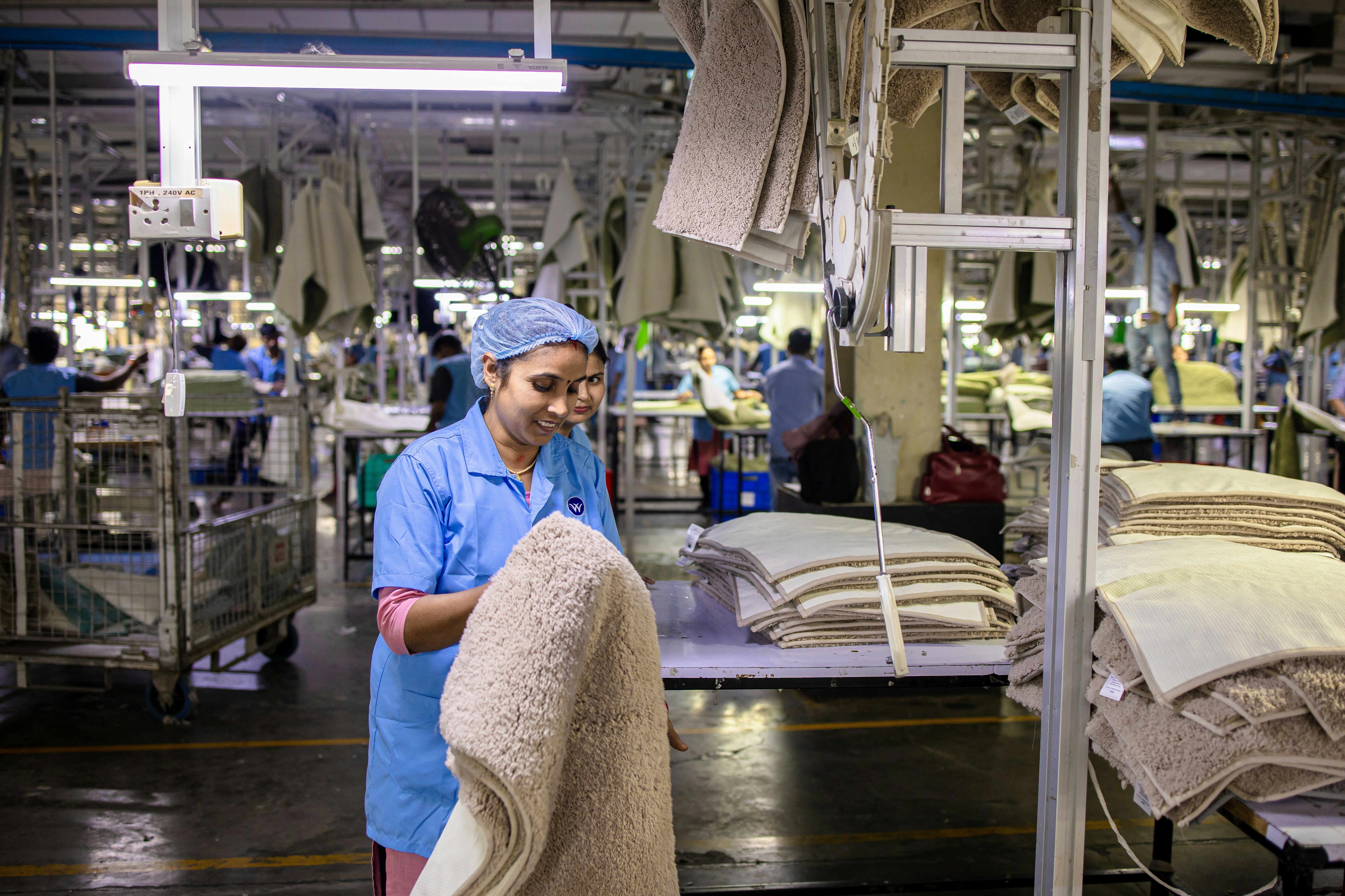 Workers are in a textile factory, manufacturing rugs.