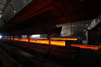 Glowing metal rods are being processed in a factory.