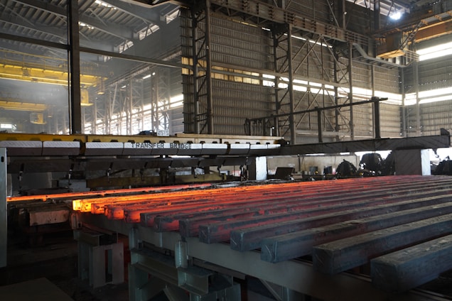 Hot metal bars are being processed in a factory.