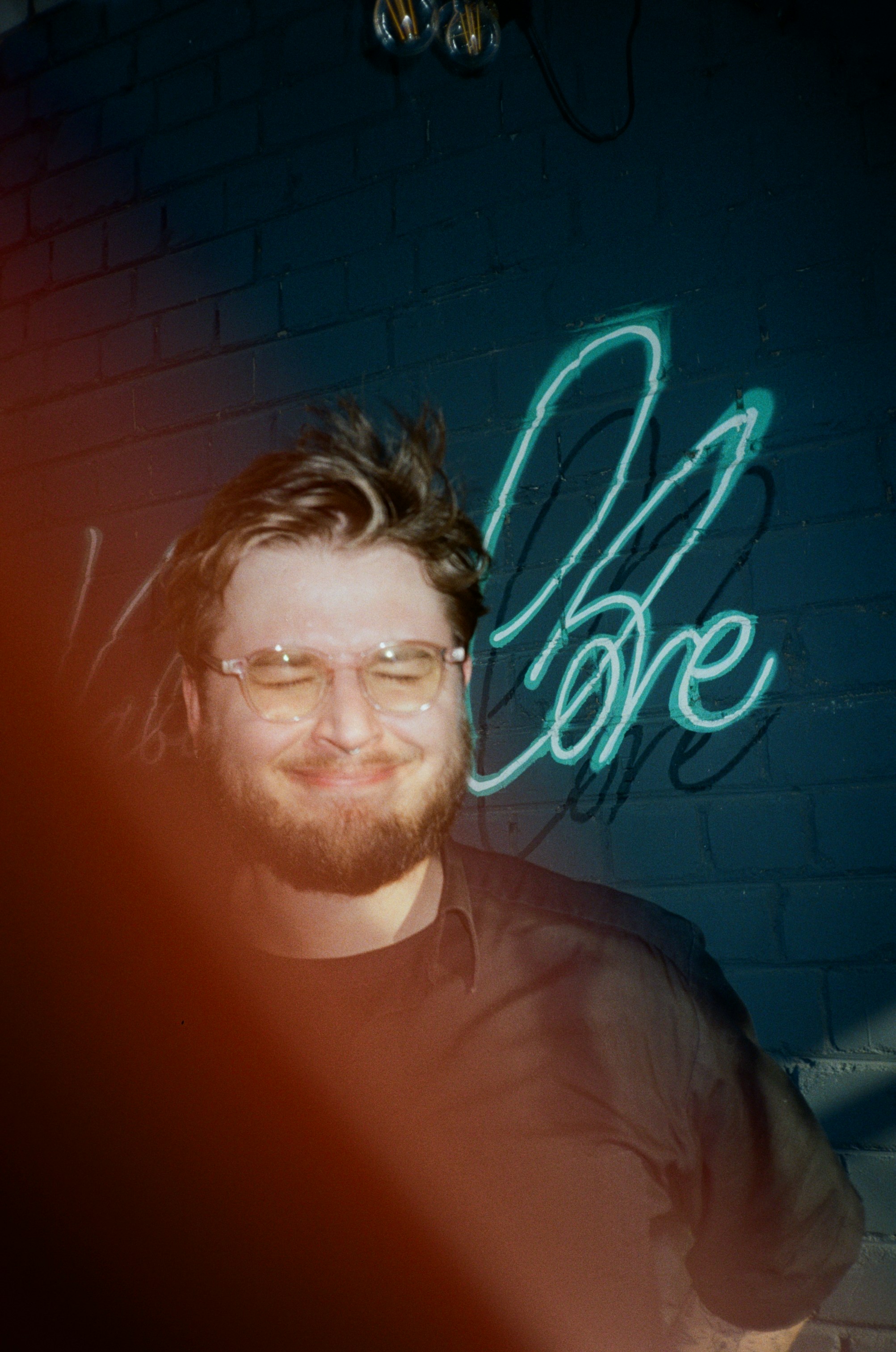 Smiling man poses in front of neon "love" sign.
