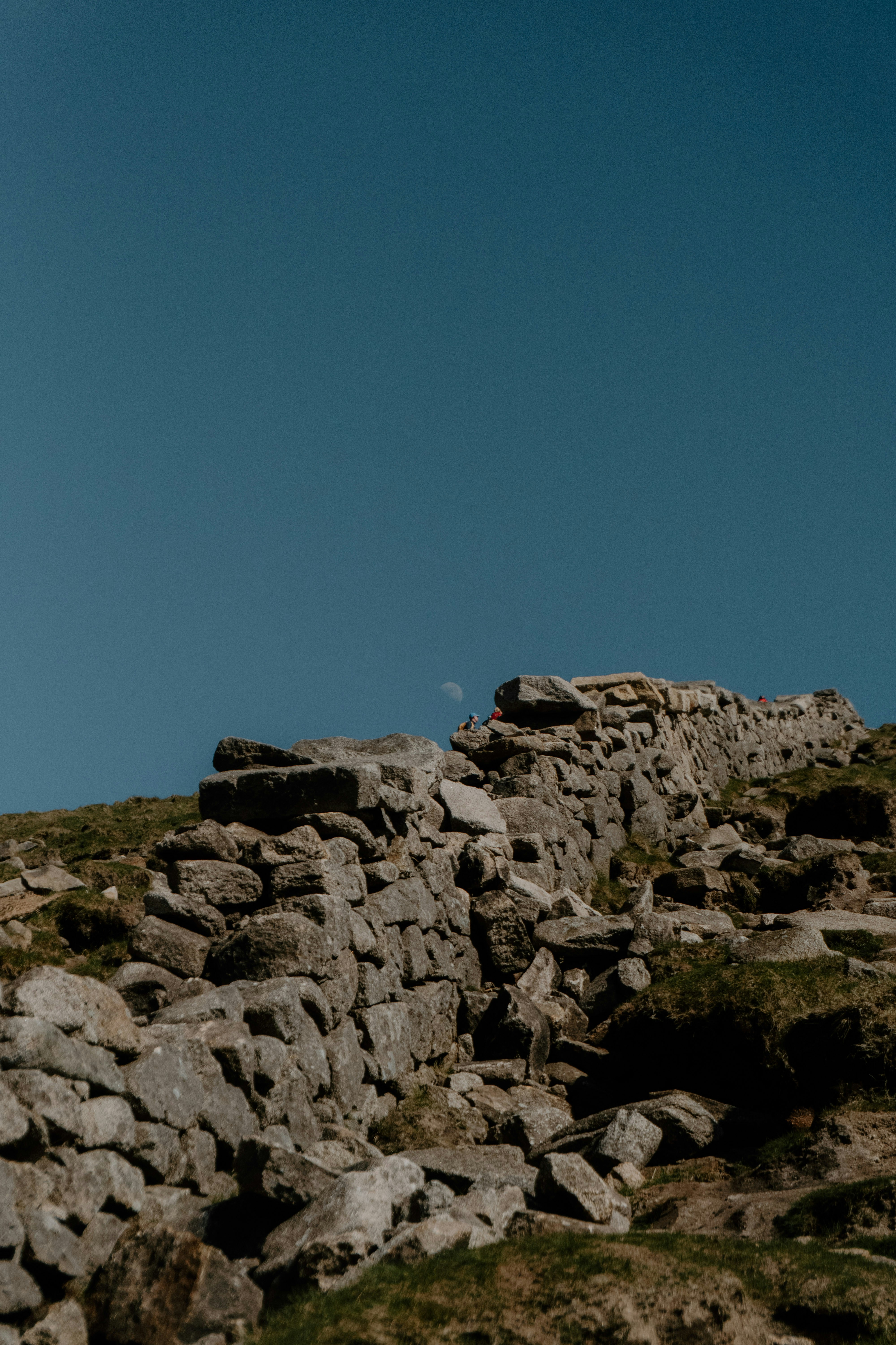 Stone wall sits on a hillside under a blue sky.