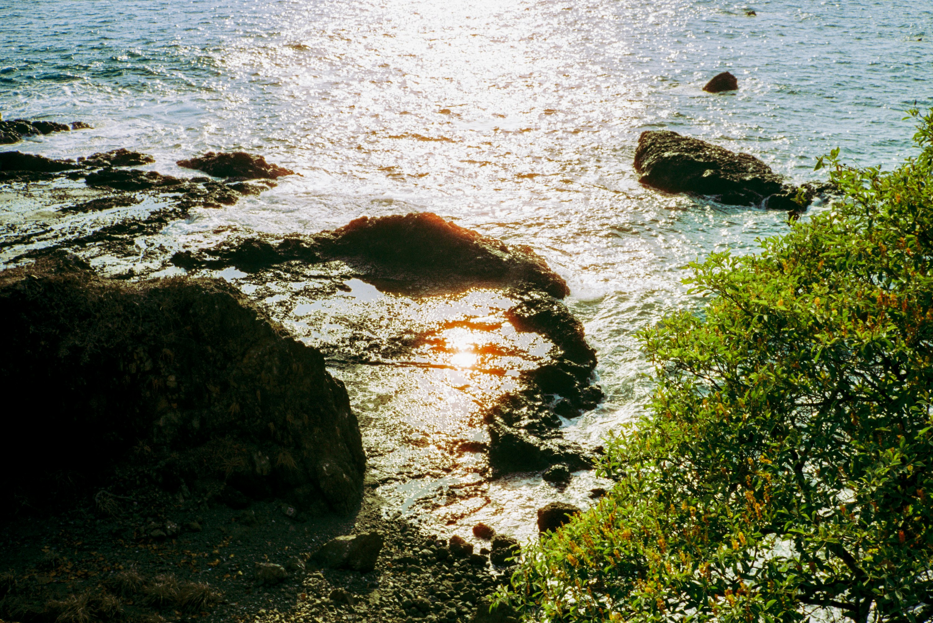Felsiges Ufer mit Sonne, die auf dem Wasser glitzert.