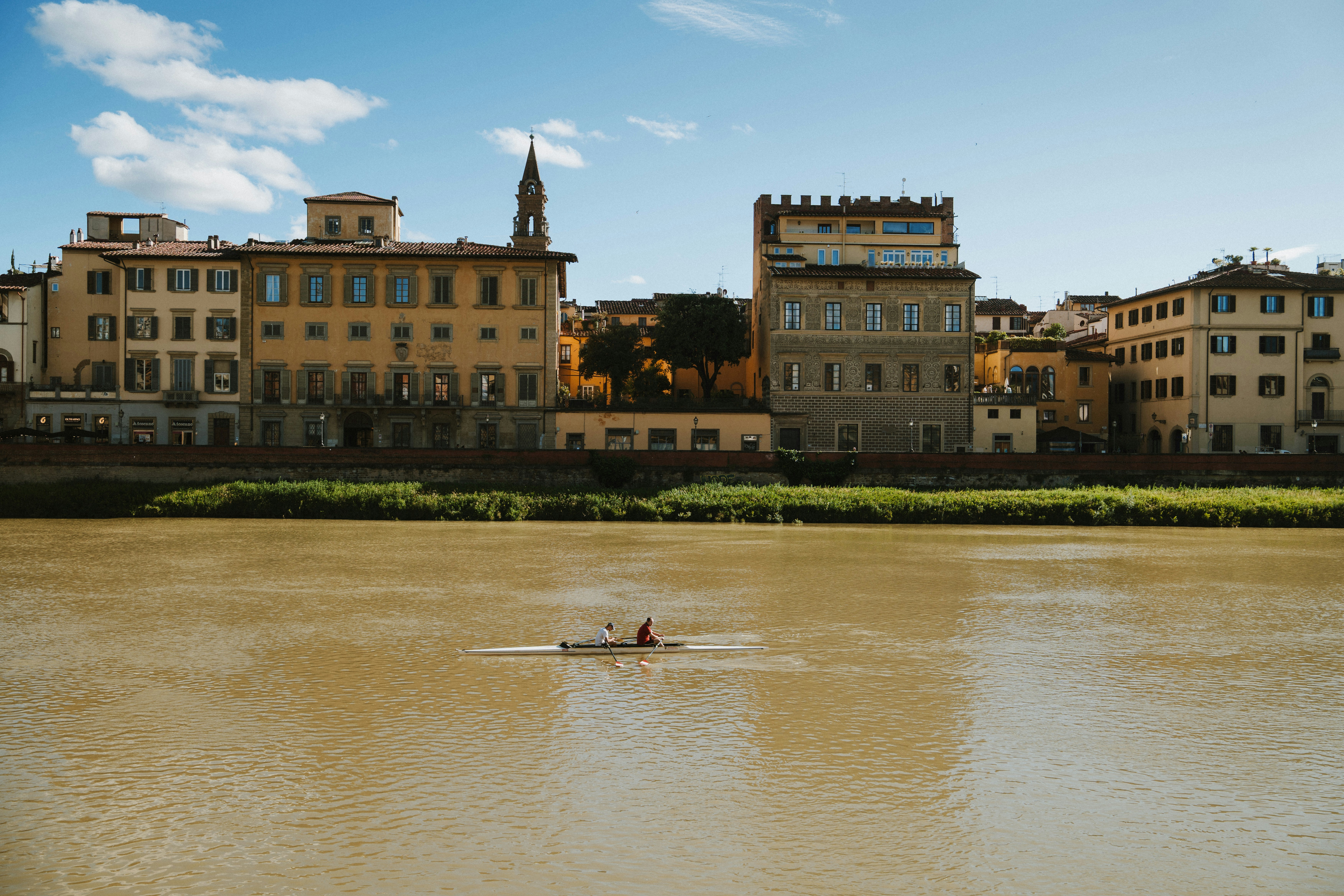 A kayaker paddles on the river under historic buildings.