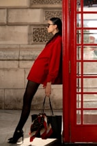 Fashionable woman poses beside a red phone booth.