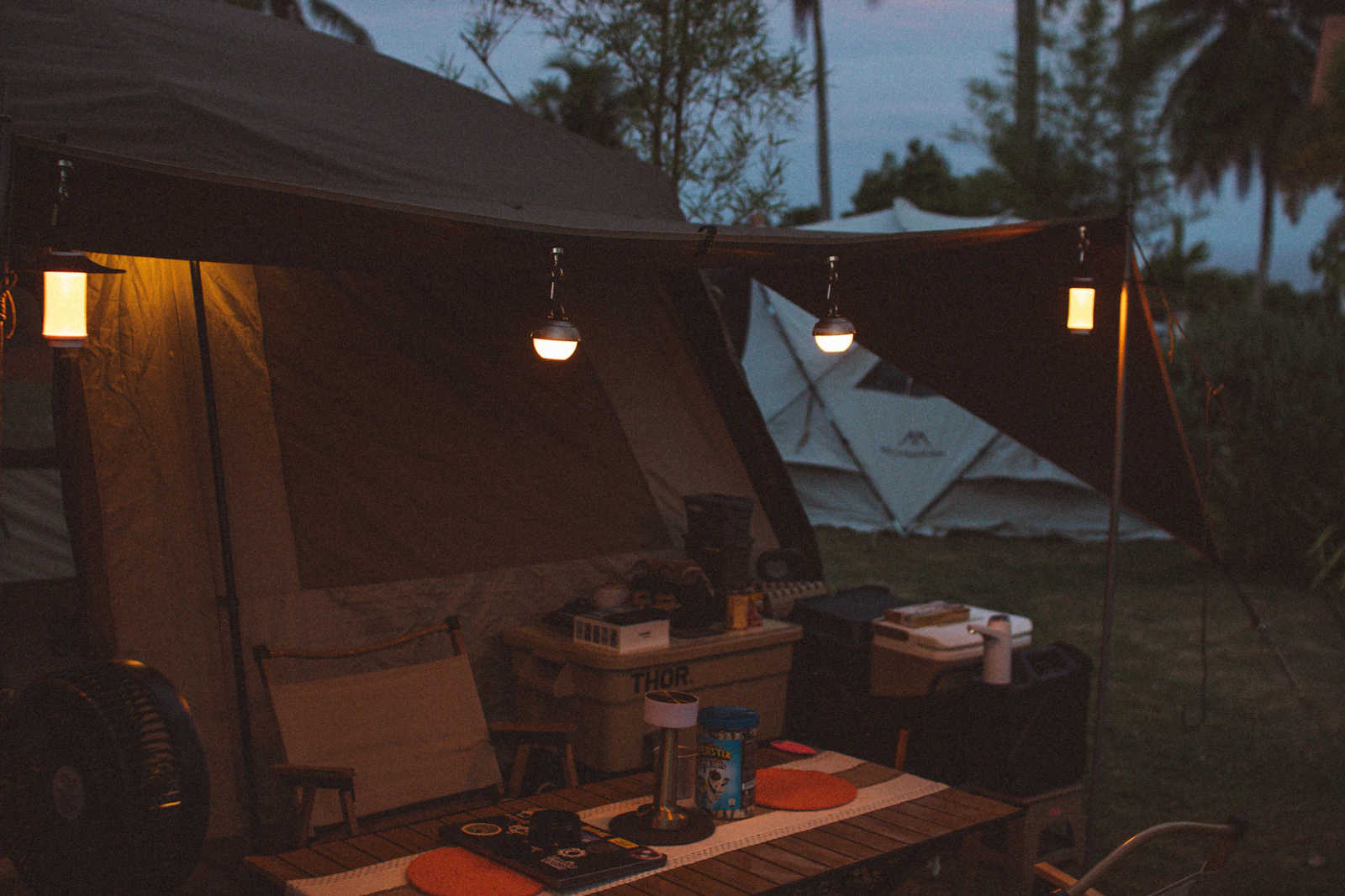 A campsite at dusk illuminated with warm hanging lanterns