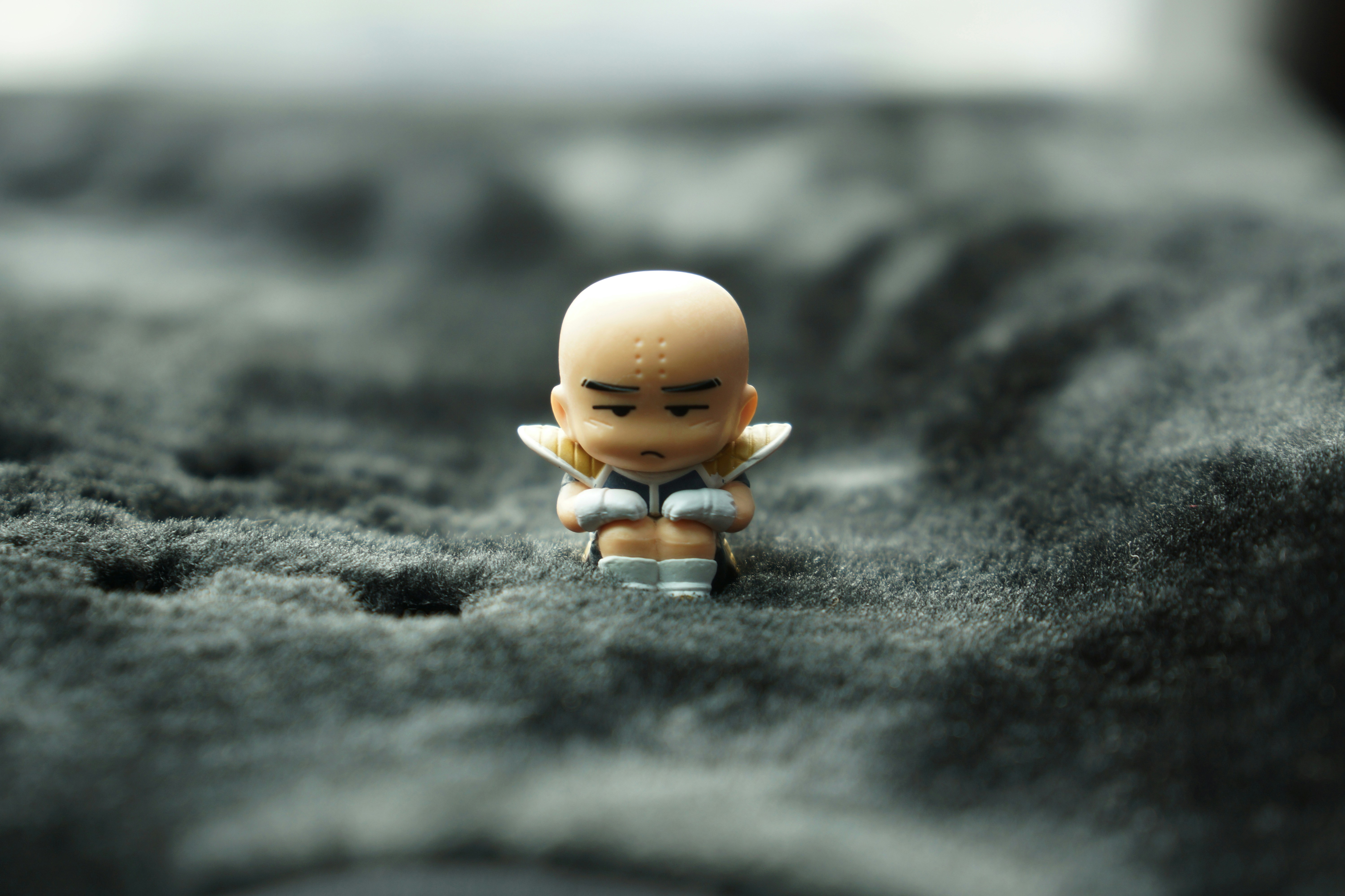 A miniature krillin figurine sits on gray fabric.
