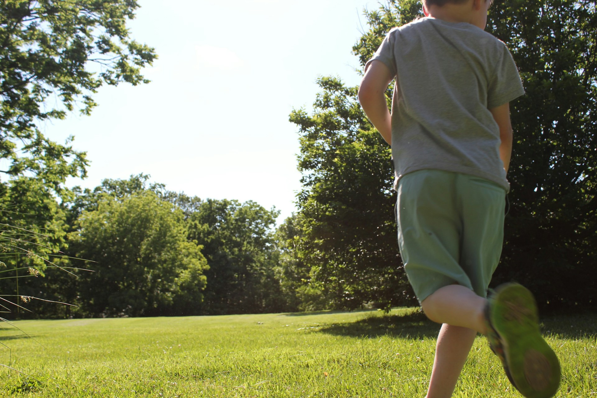 A boy runs across a green, sunny field.