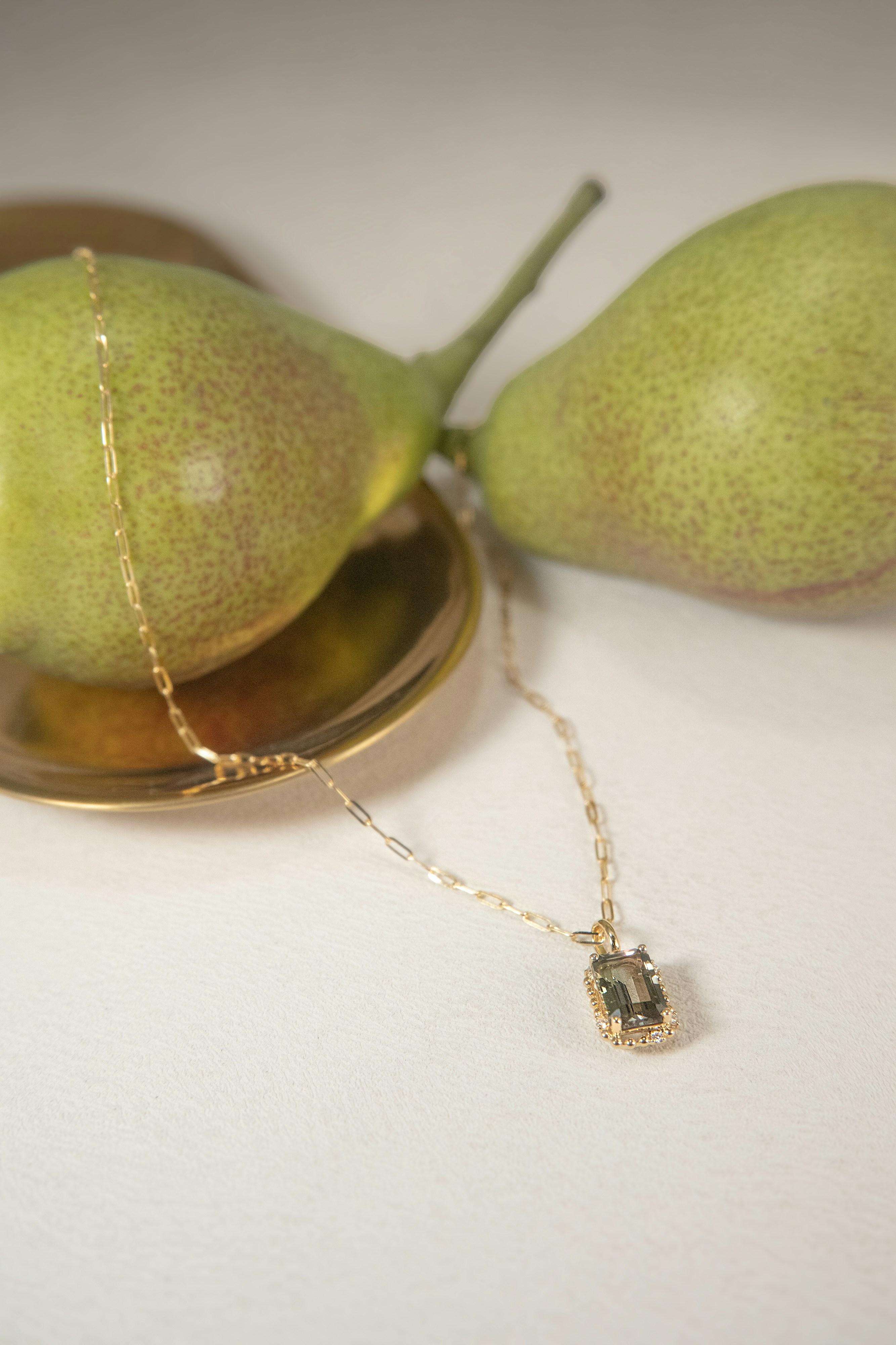 Eine Halskette ruht neben Birnen auf einem Teller.