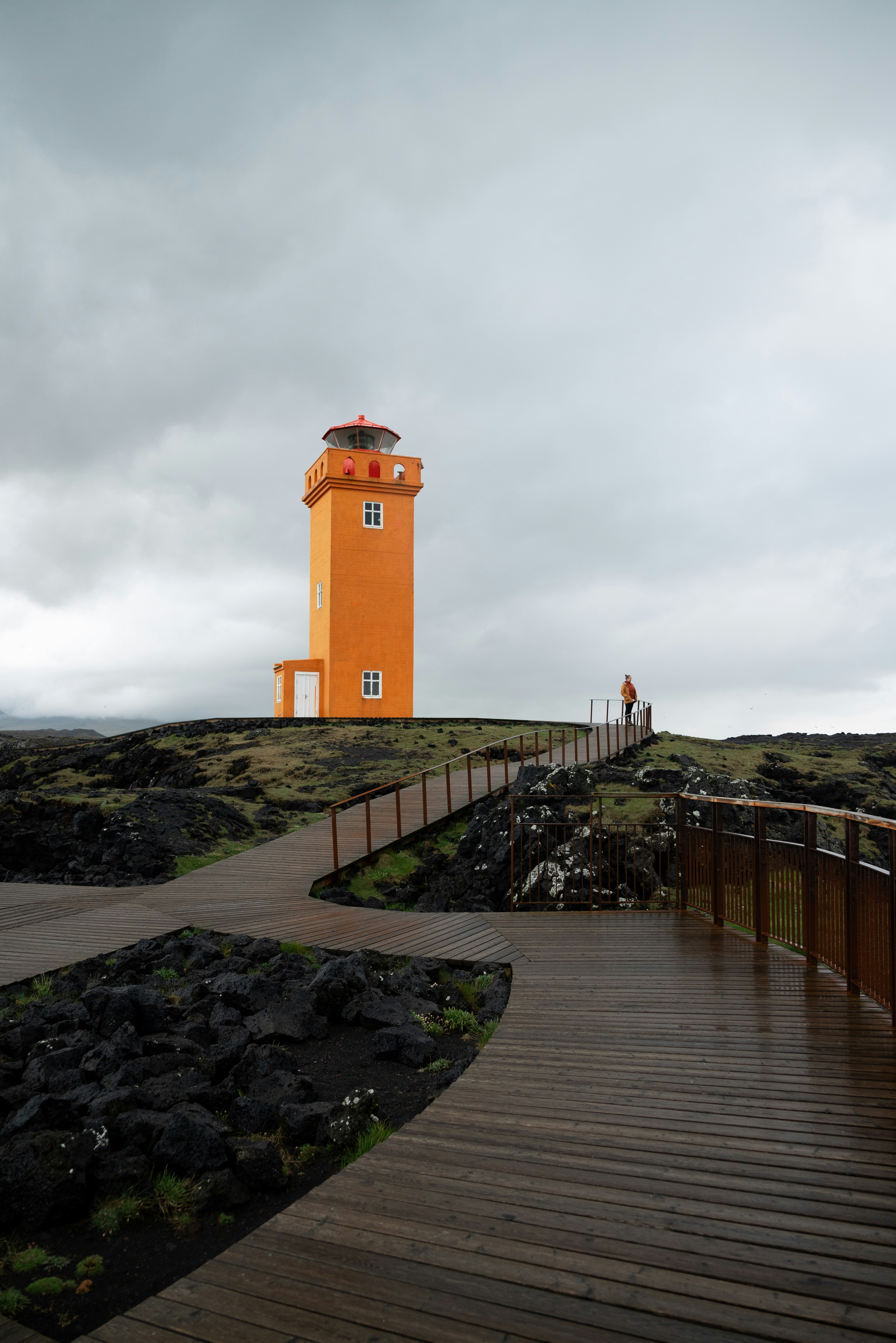 A bright orange lighthouse stands under cloudy skies.