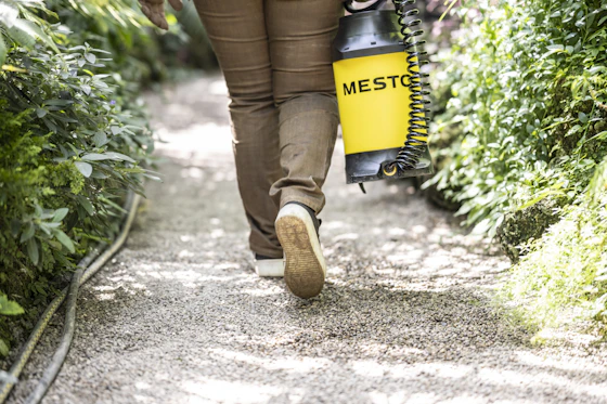 Technician carrying a backpack sprayer along a garden path