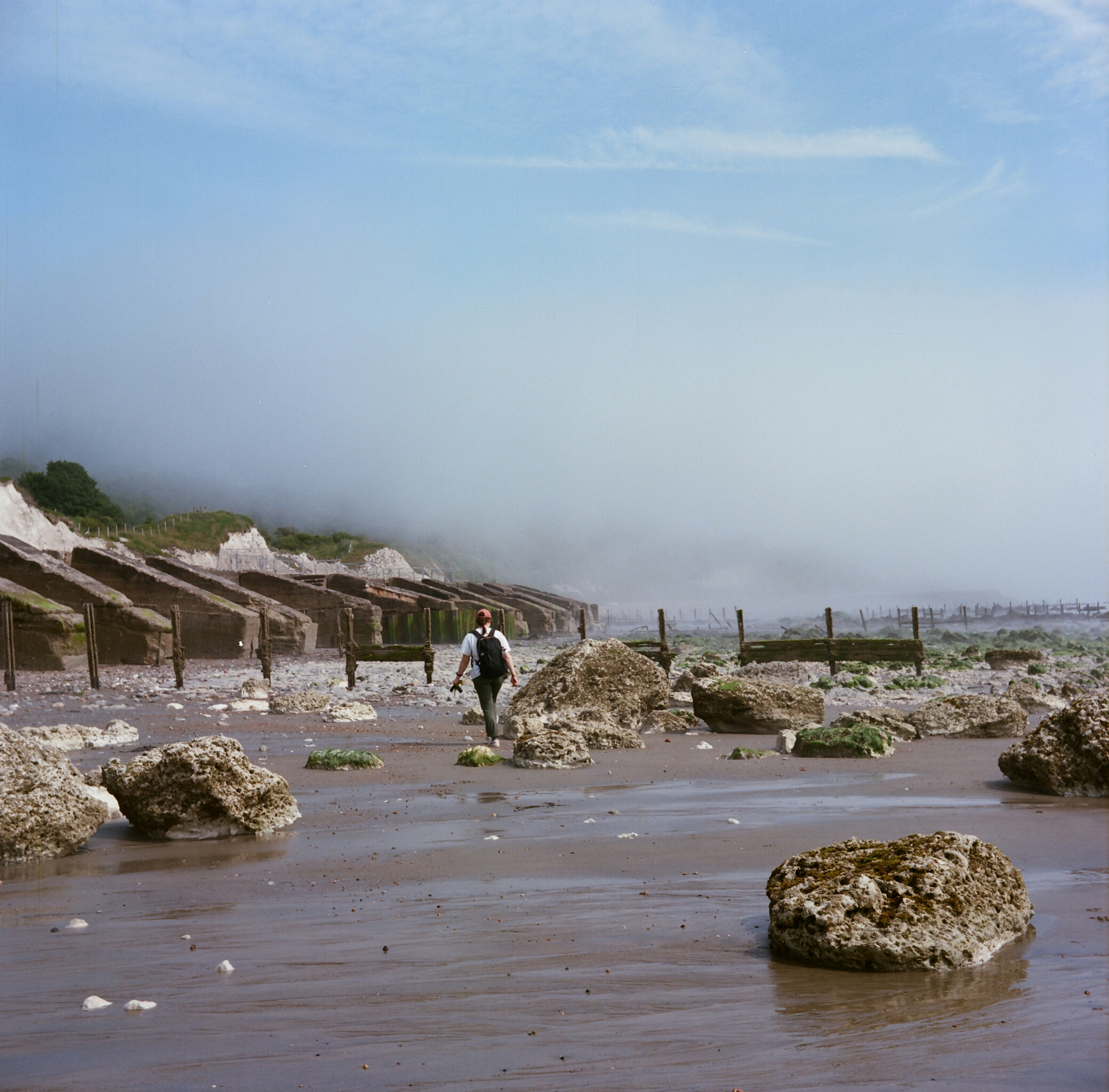 Person walks on a beach with fog present.