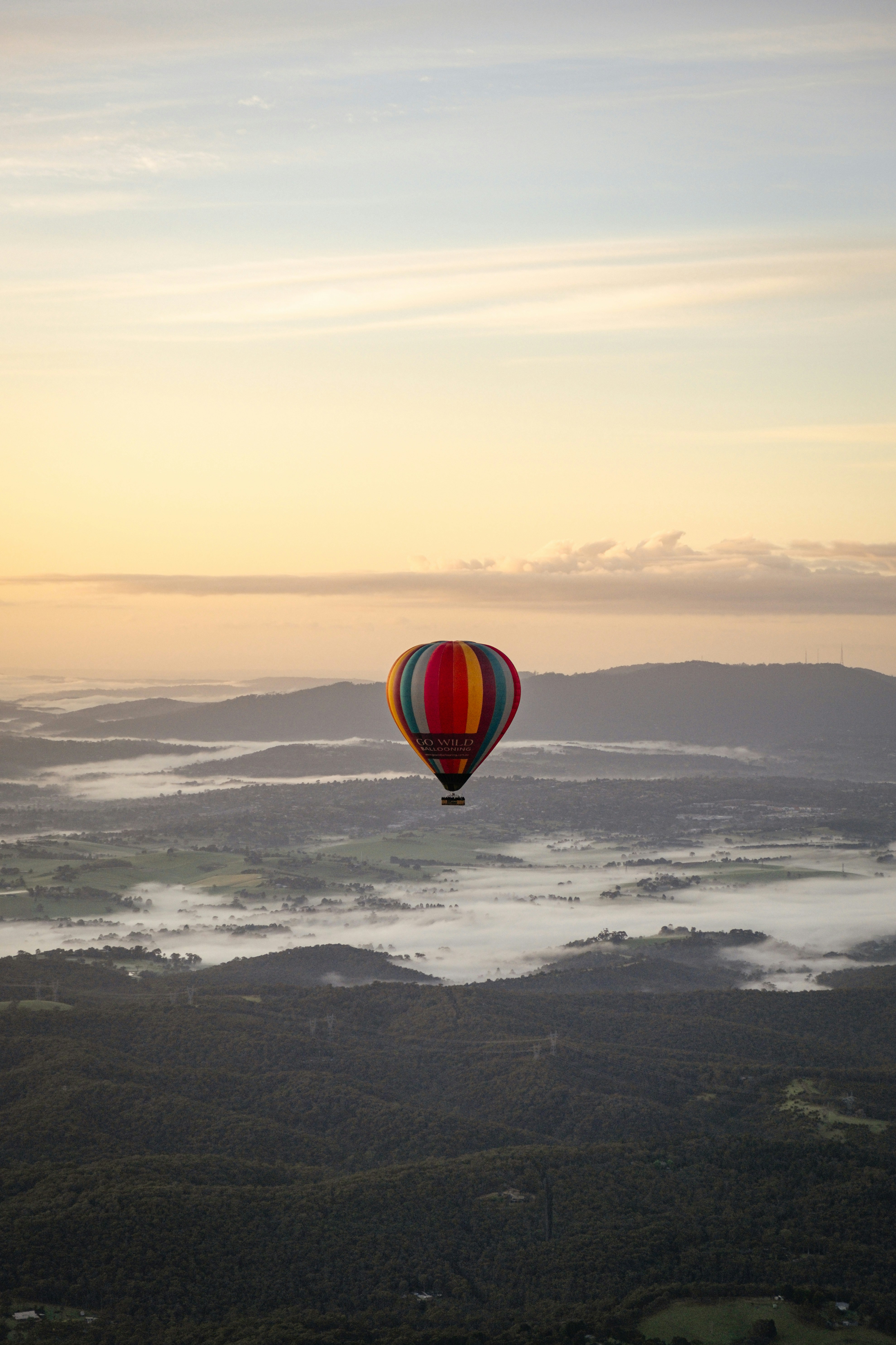A hot air balloon floats over misty mountains.