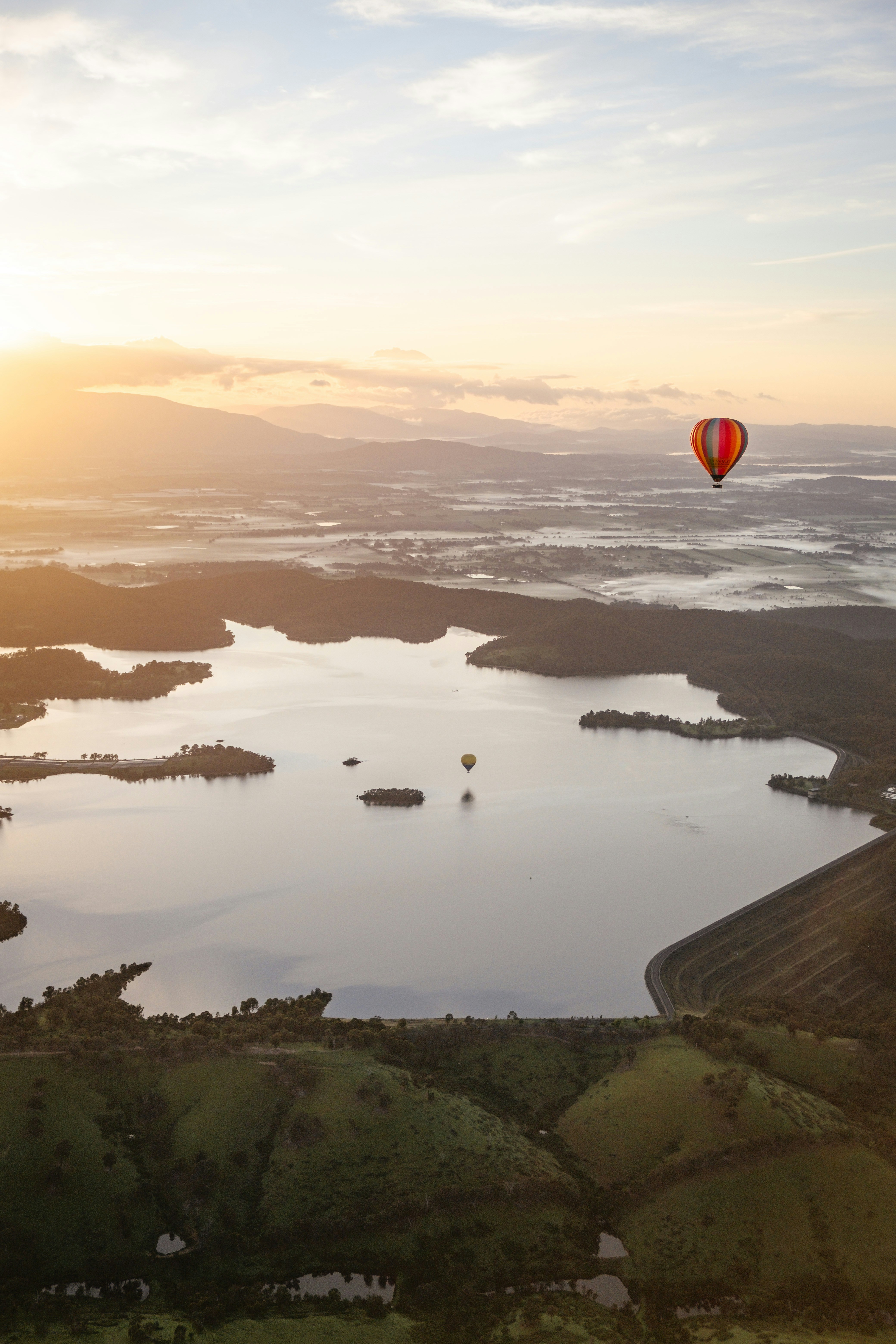Hot air balloons fly over a serene lake at sunrise.
