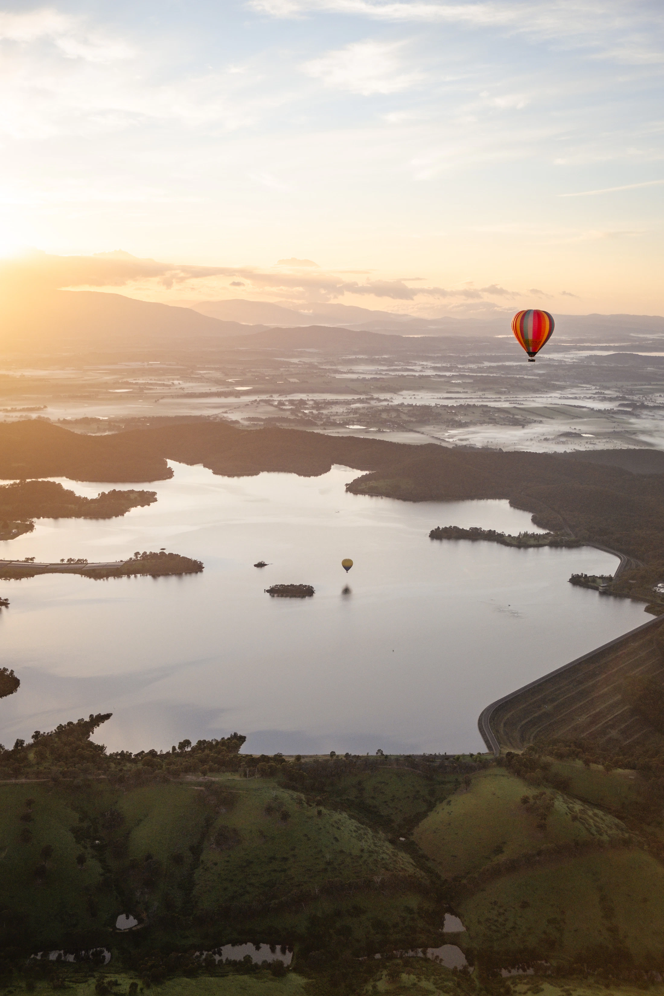 Hot air balloons gliding over a misty lake in early morning light