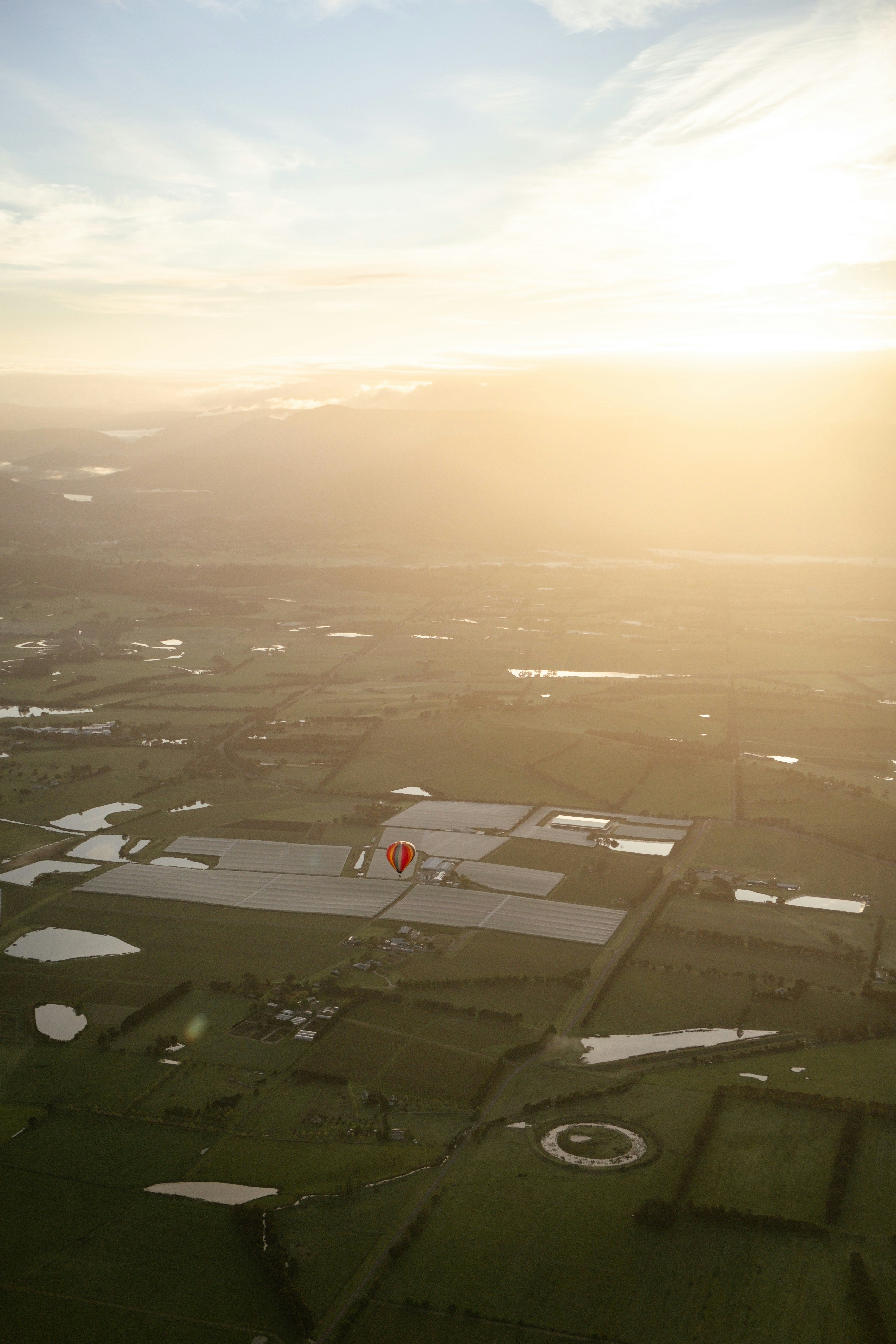 A hot air balloon floats over green fields at sunset.