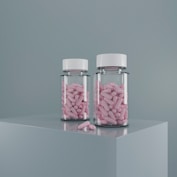 Two pill bottles filled with pink medication.