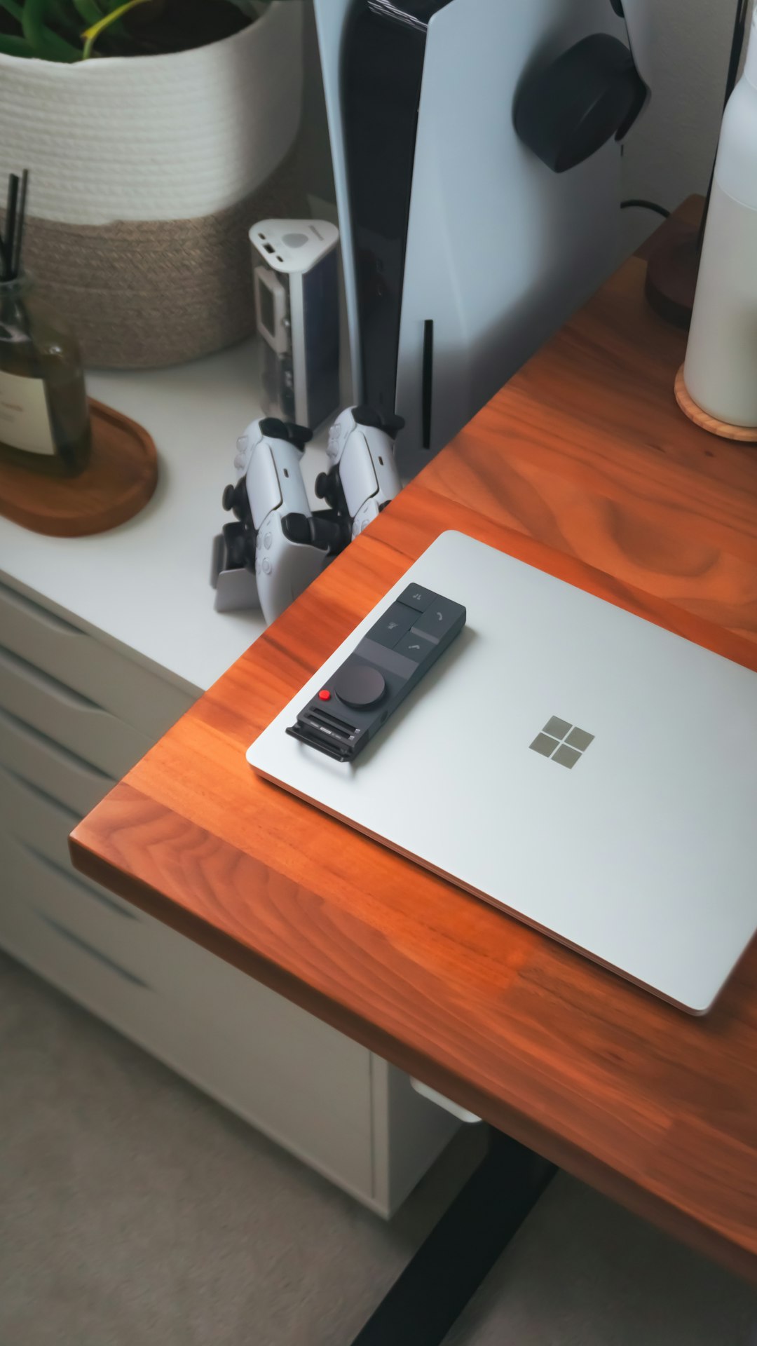 Laptop, remote, and playstation setup on a desk.