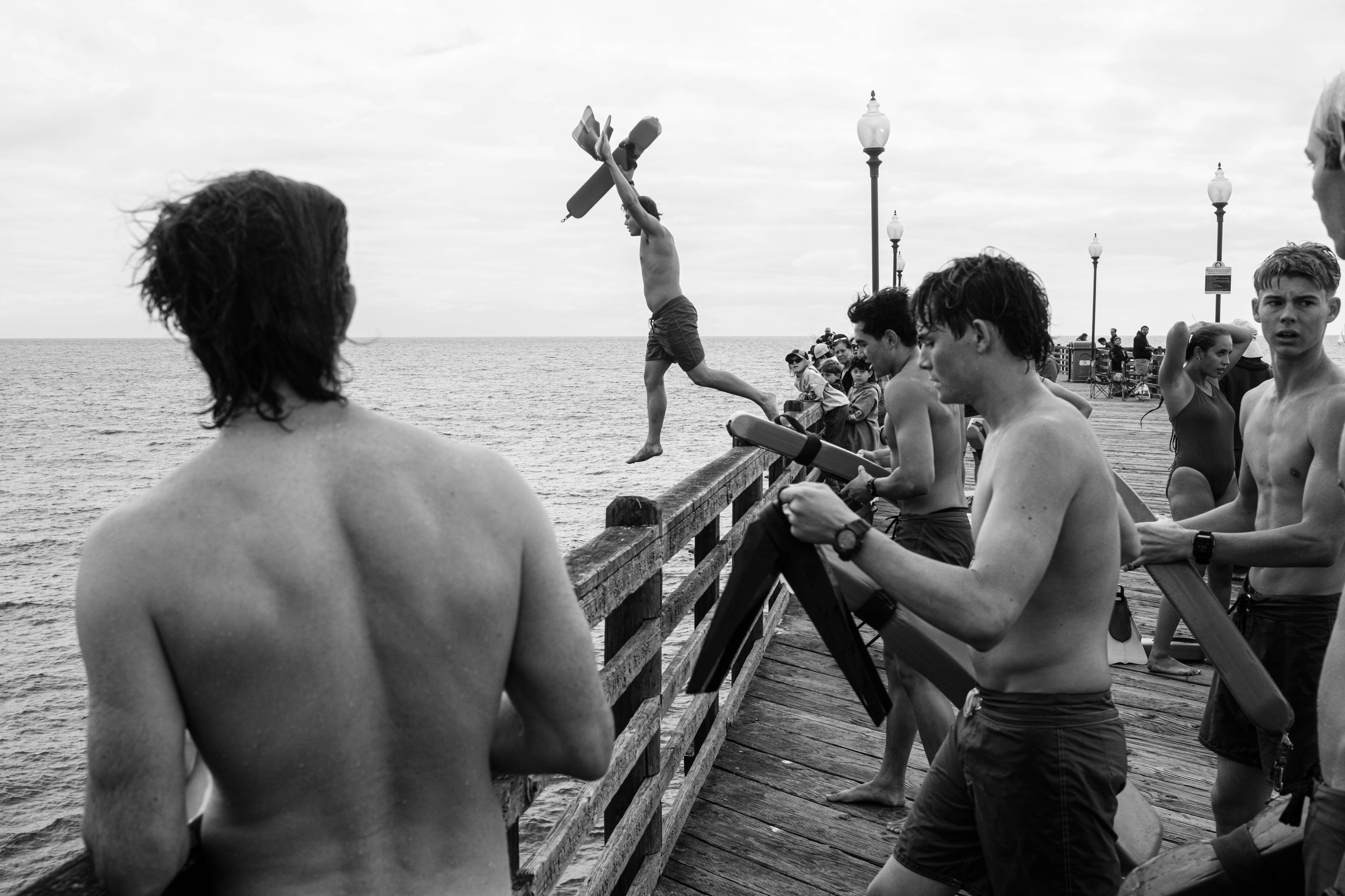 Boys enjoy jumping off a pier into the ocean.