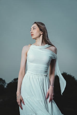 Woman in white dress looks thoughtfully away.