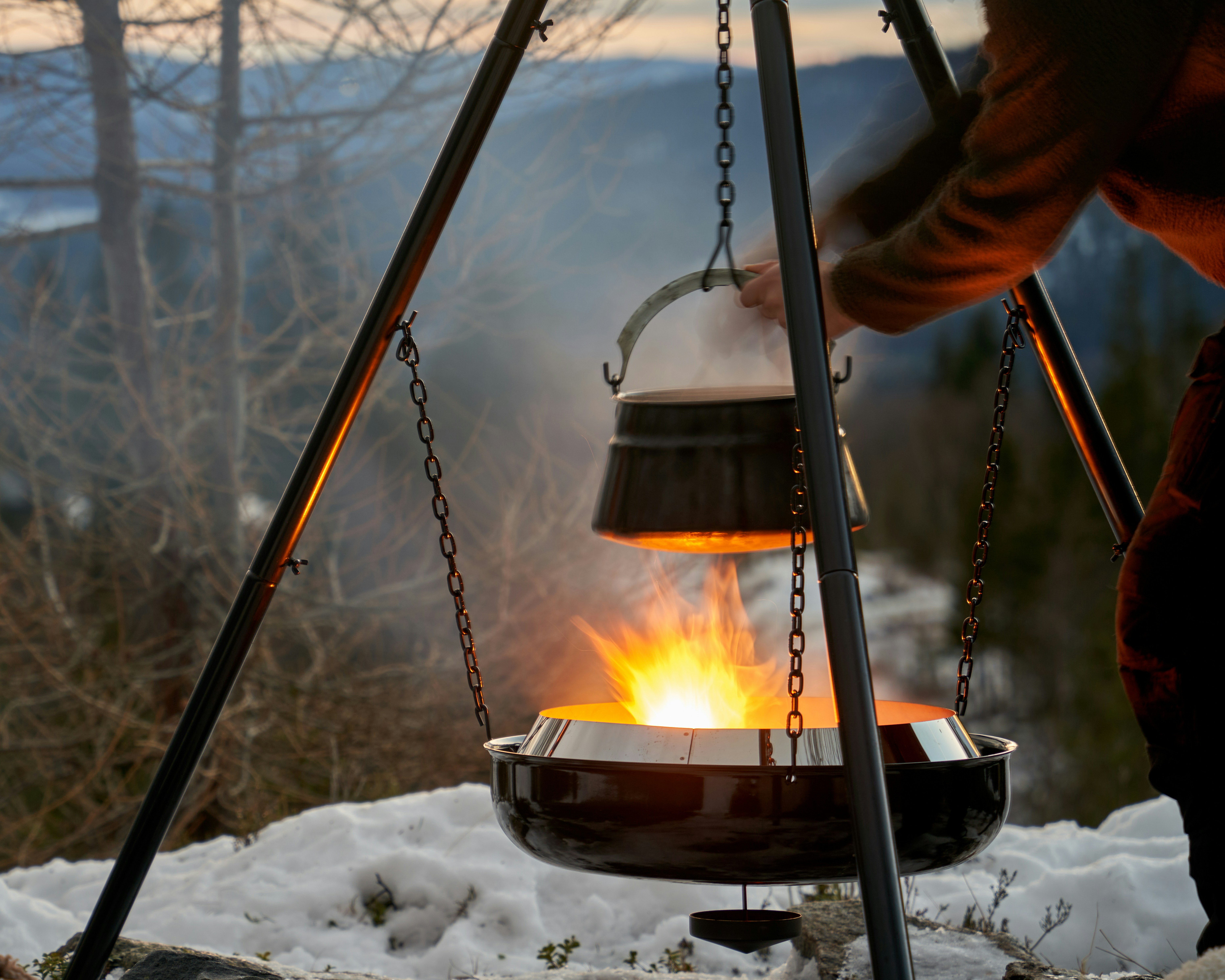 Talvine lõkkekokkamine matkal – pott ripub lõkke kohal mägede taustal