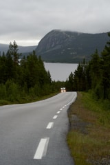 A car travels down a road near a lake.