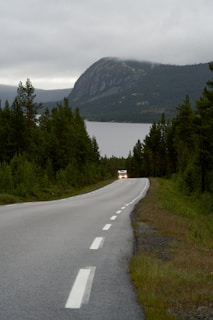 A car travels down a road near a lake.