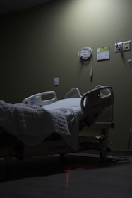 An empty hospital bed sits in a dimly lit room.