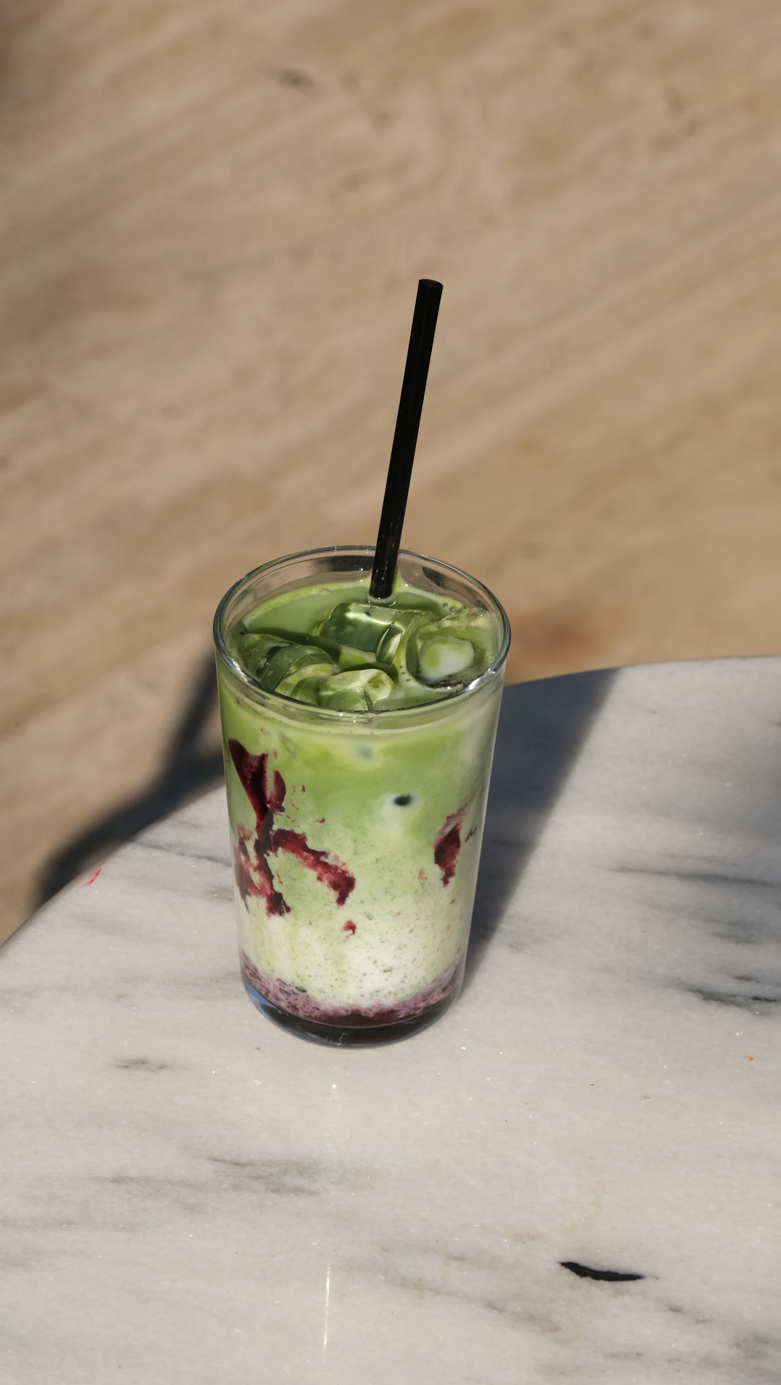 A glass of iced matcha latte with a dark berry layer on a marble surface