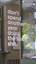 White lettering reading "don't spend another year doing the same shit" on a glass door