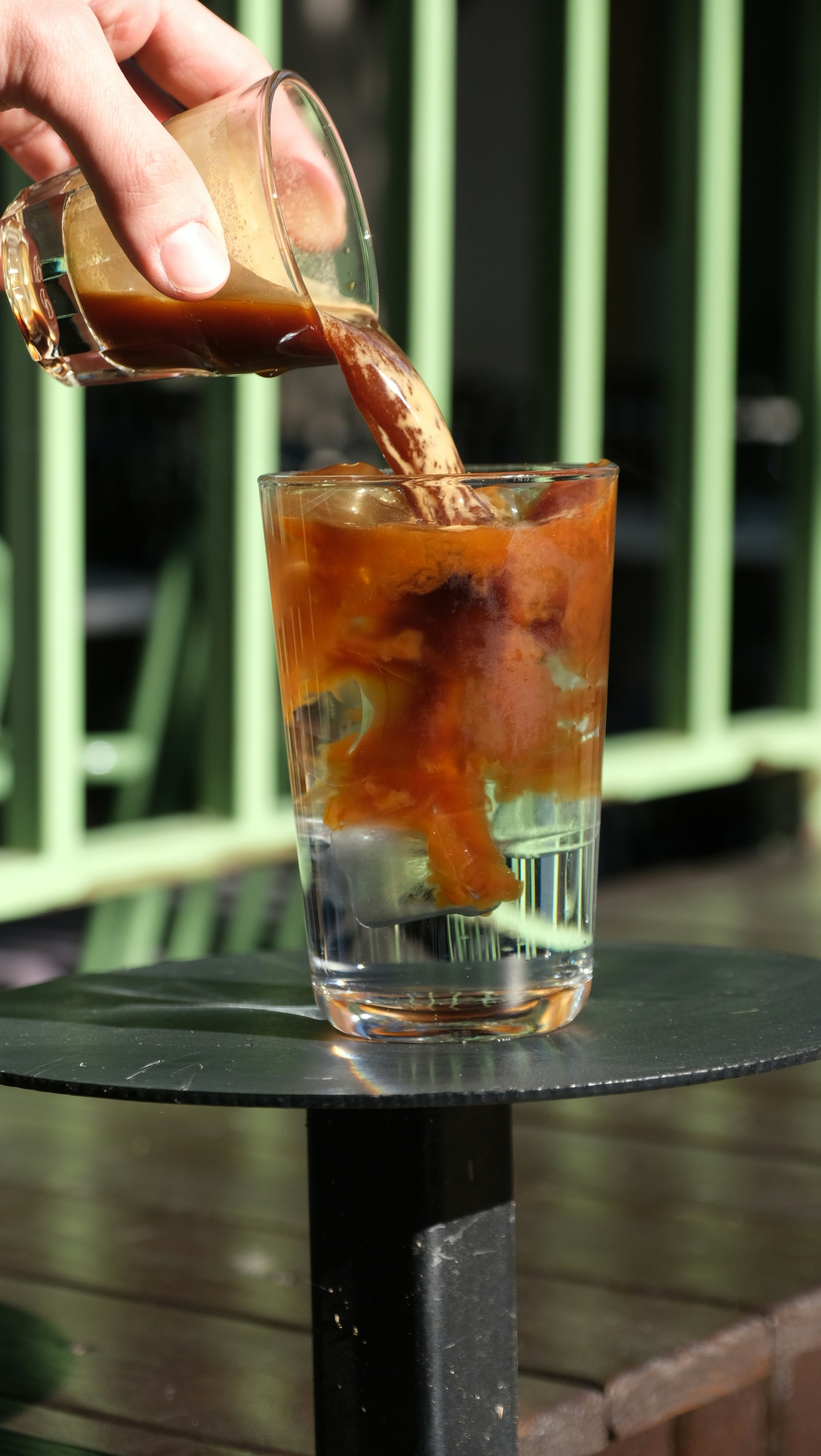 Coffee is being poured into a glass of water.