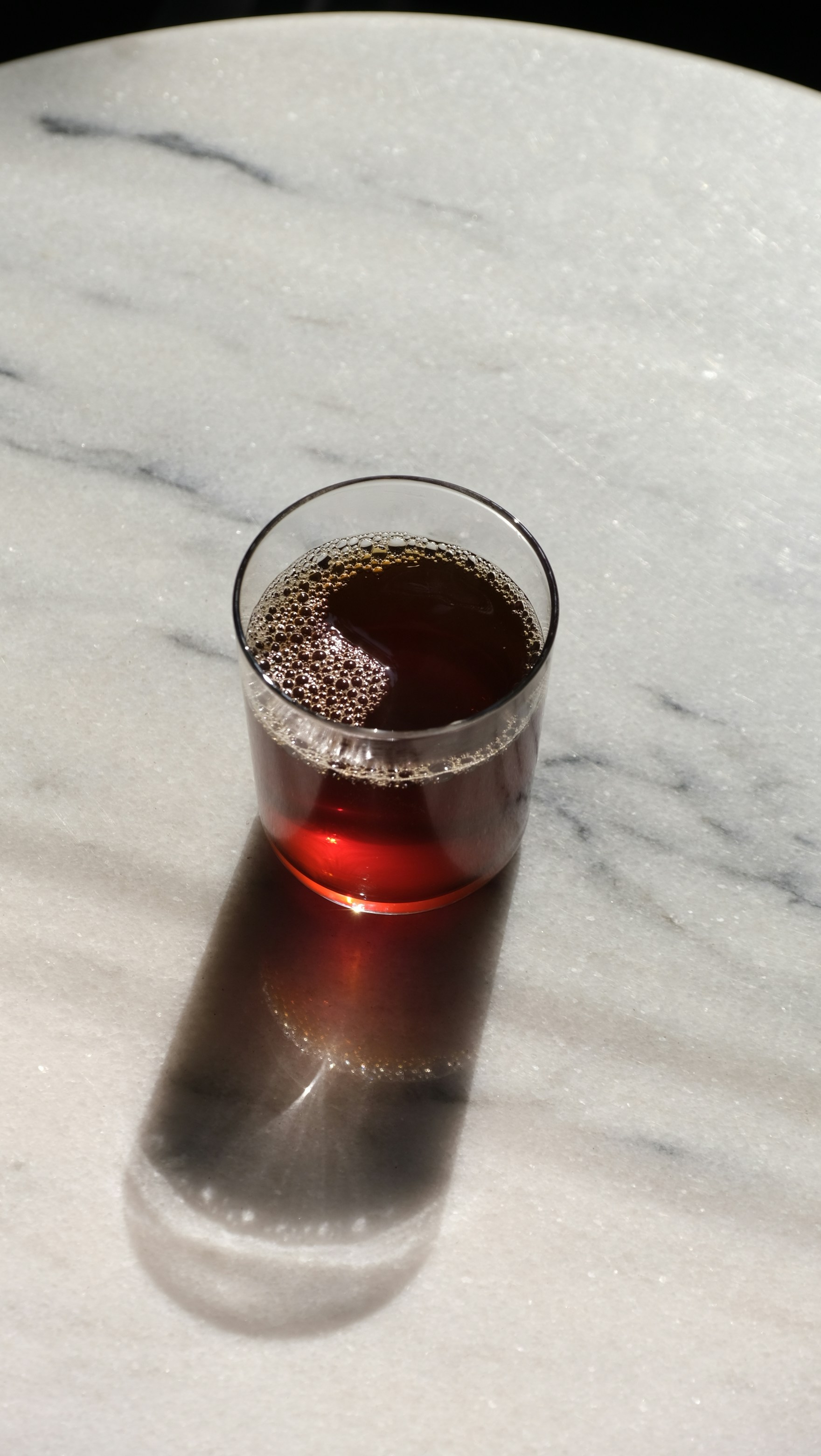 A glass of dark liquid on a marble surface.