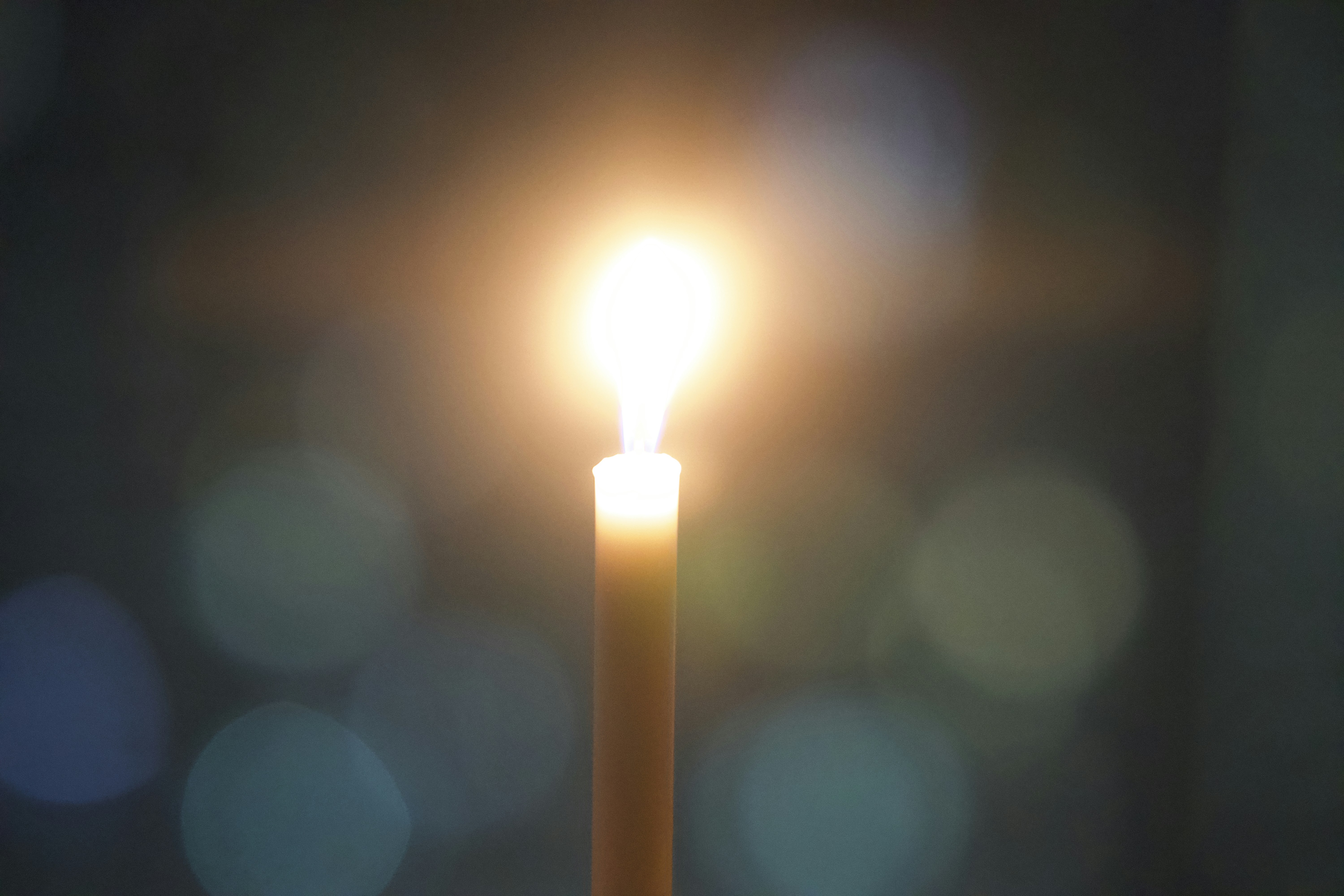 A lit candle shines bright against blurred lights.