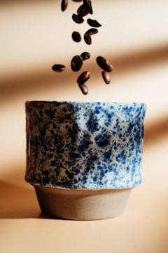 Coffee beans are falling into a ceramic cup.
