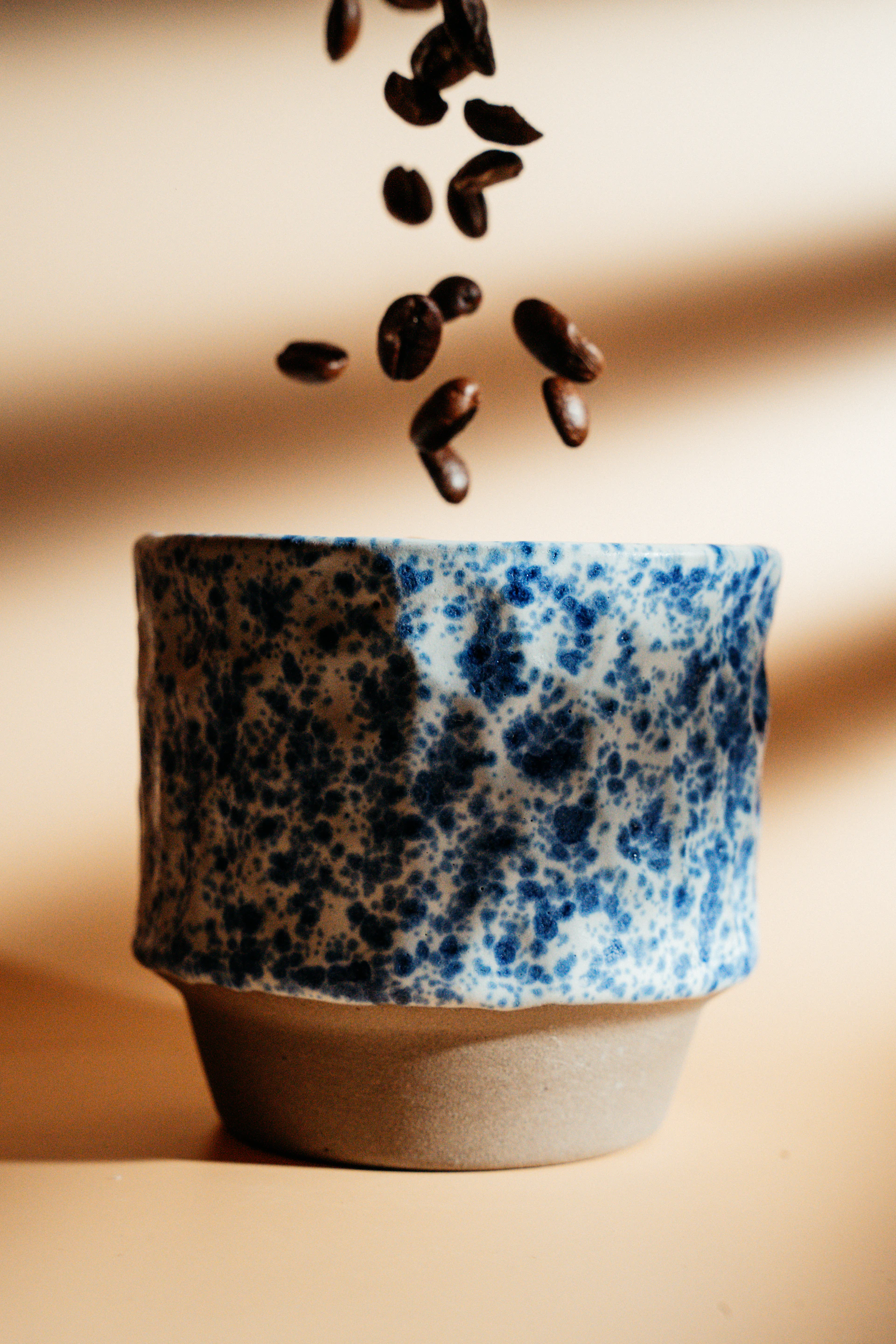 Coffee beans are falling into a ceramic cup.