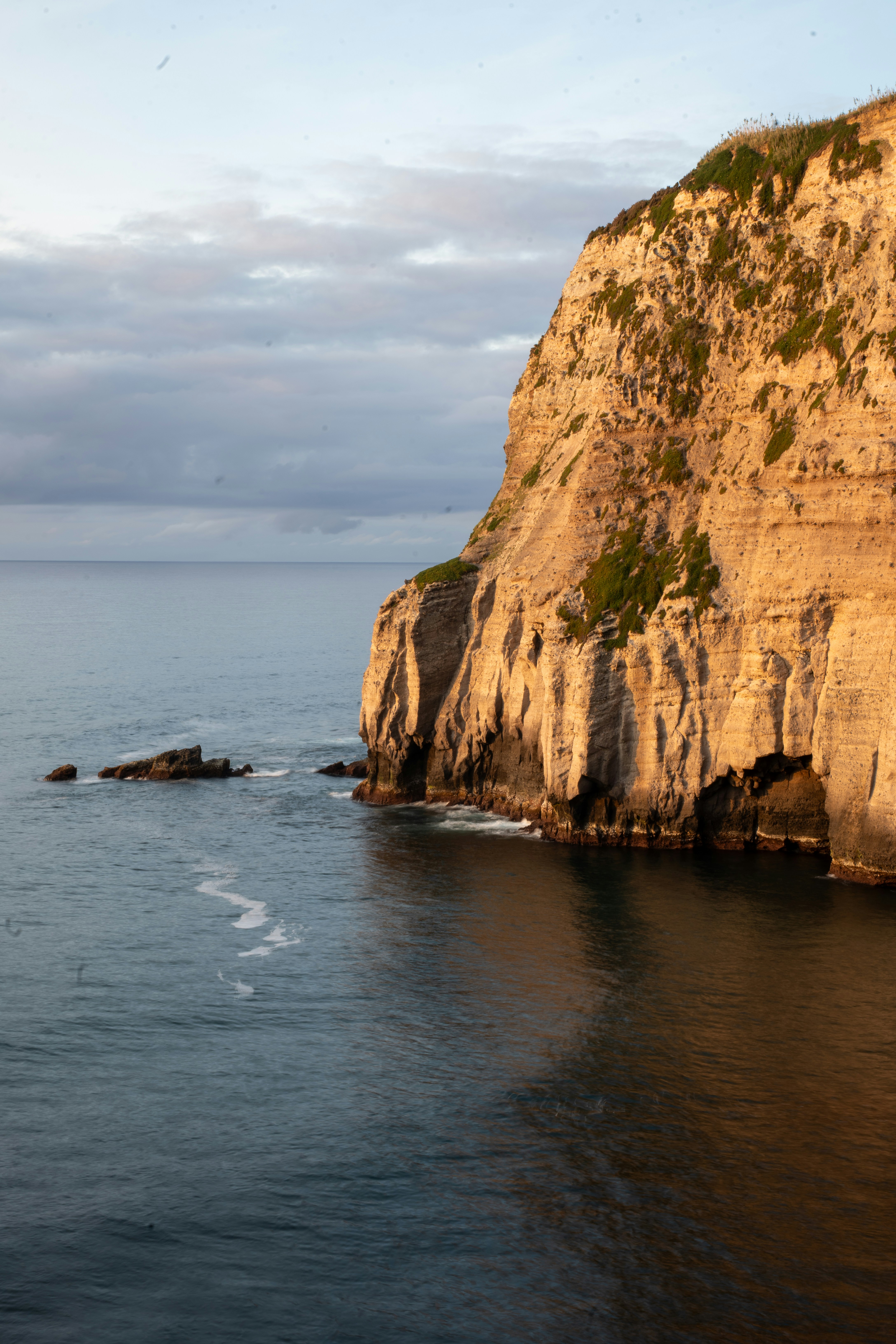 Cliffside meets the ocean under a cloudy sky.