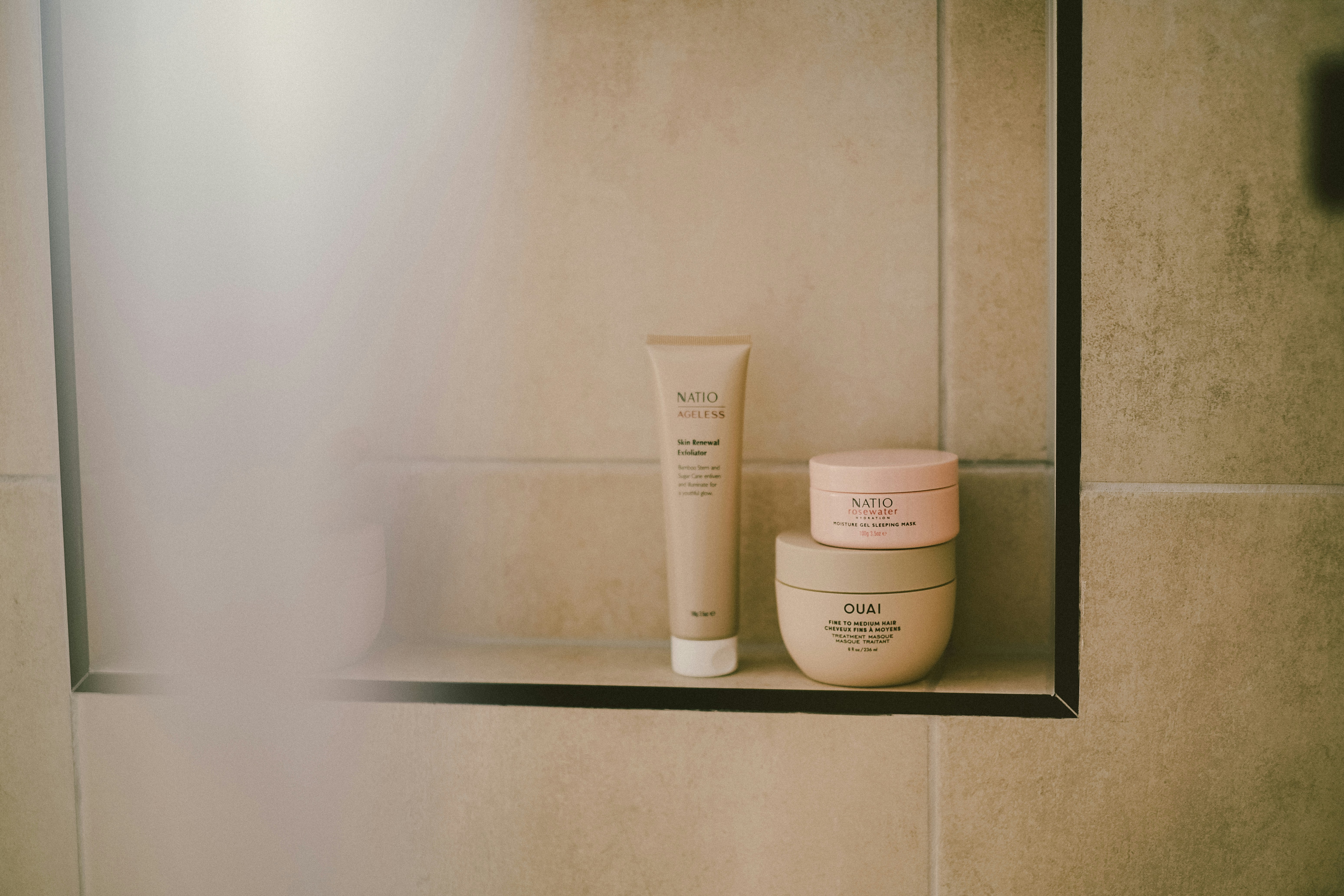 Skincare products sit on a shelf in a shower.