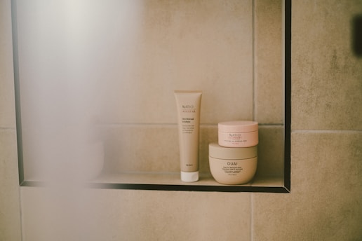 Skincare products sit on a shelf in a shower.