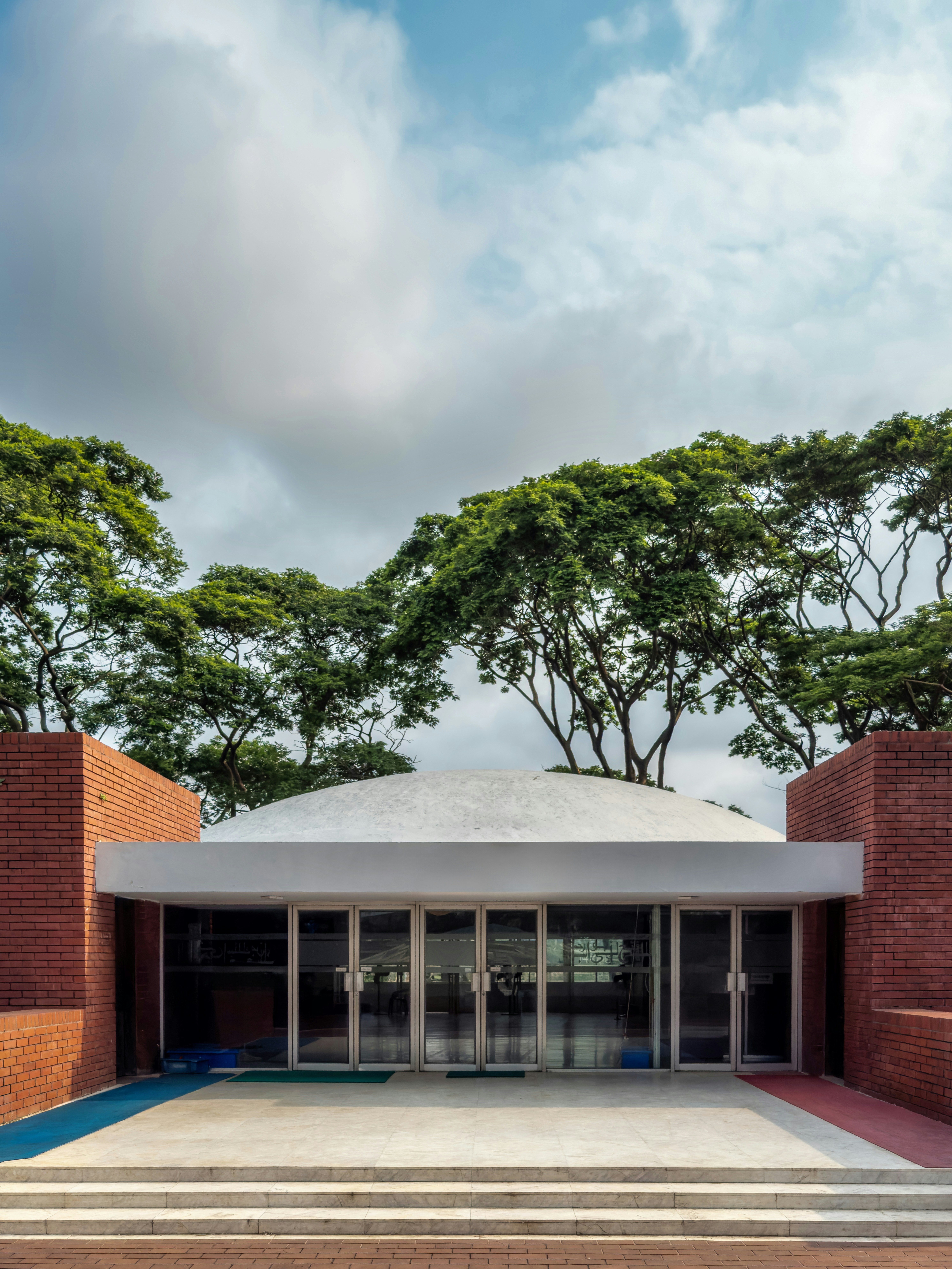 Moderne Gebäudefassade mit Bäumen und bewölktem Himmel.