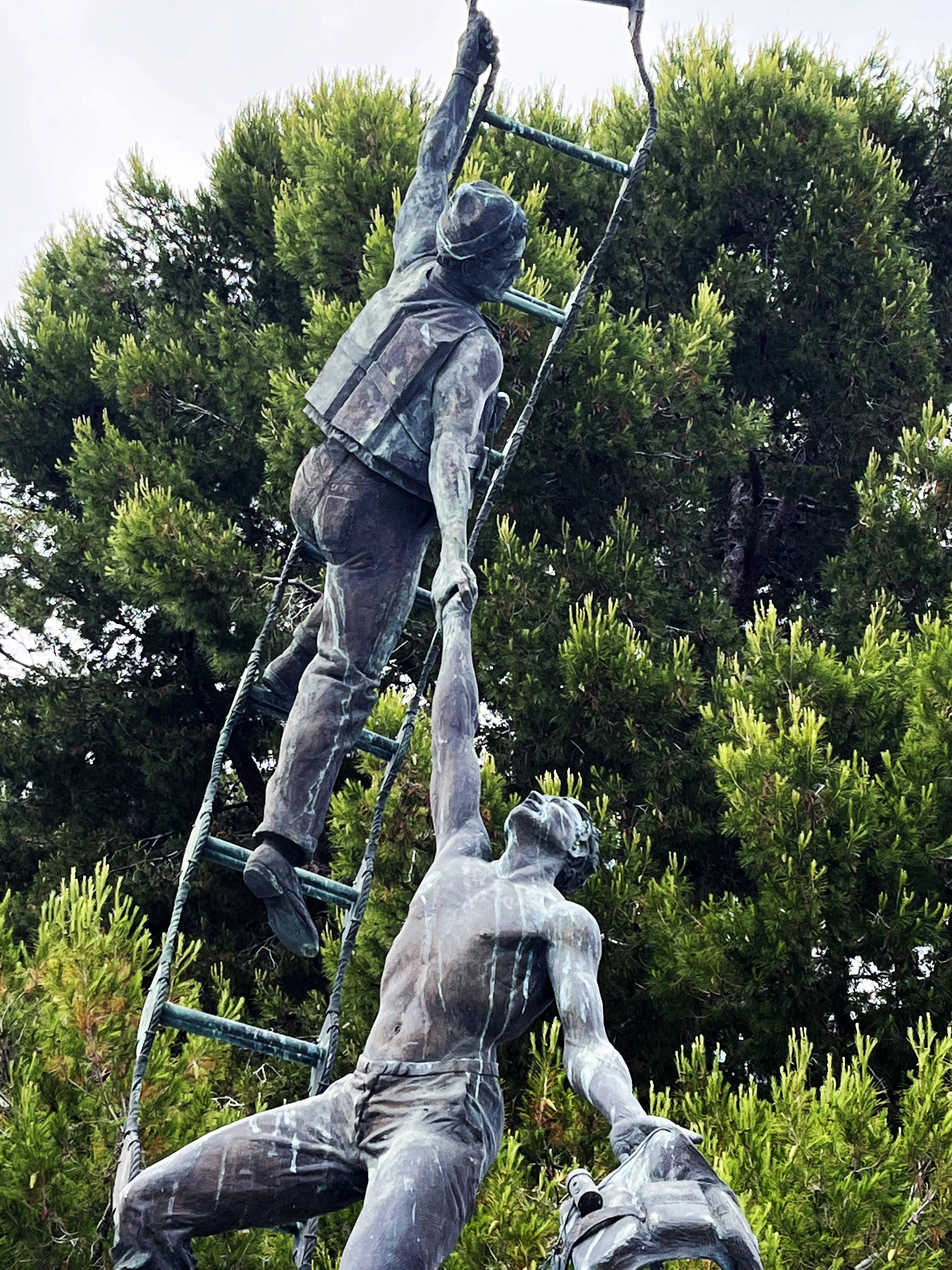 Sculpture depicts two men helping each other on a ladder.