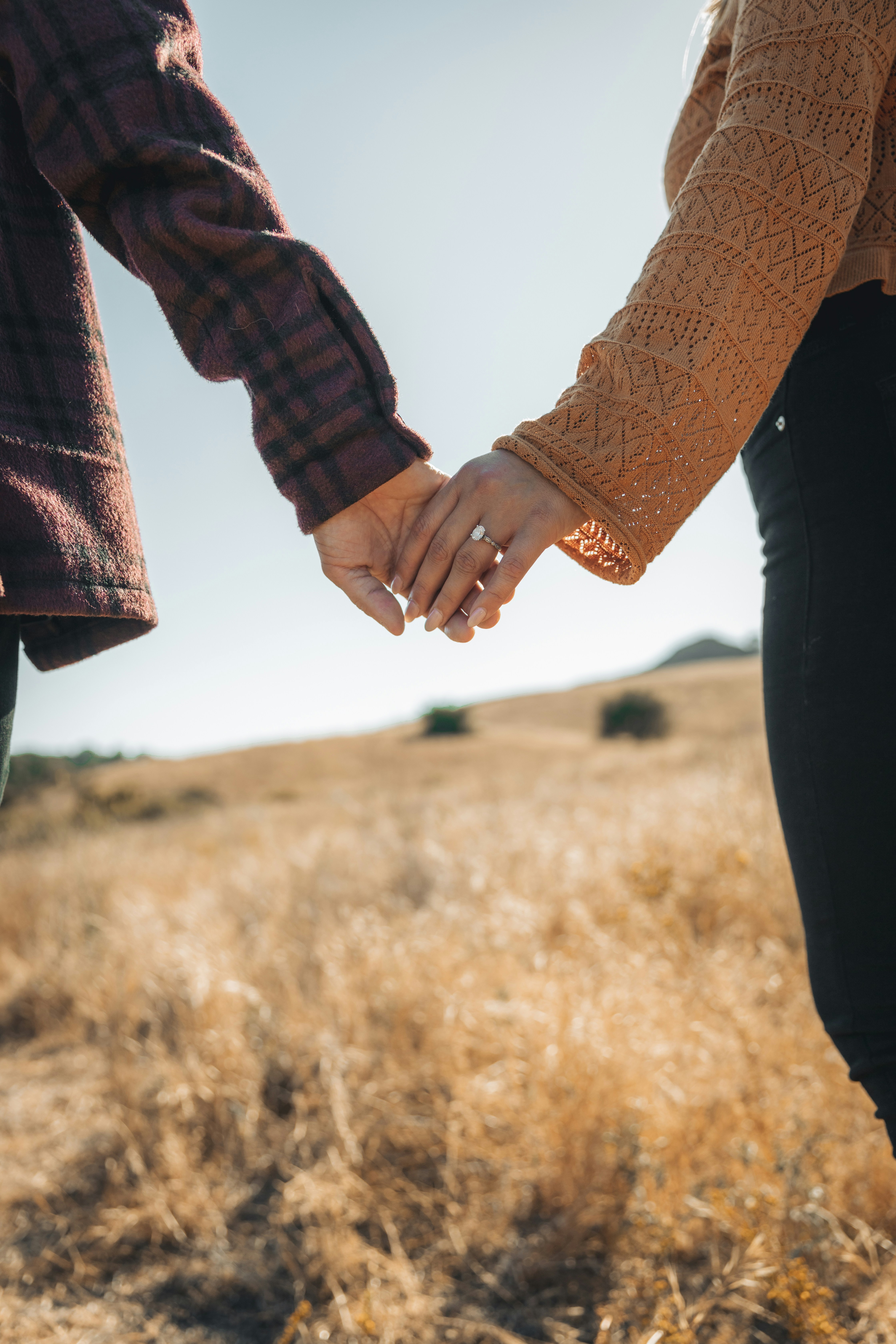 A couple holds hands in a grassy field.